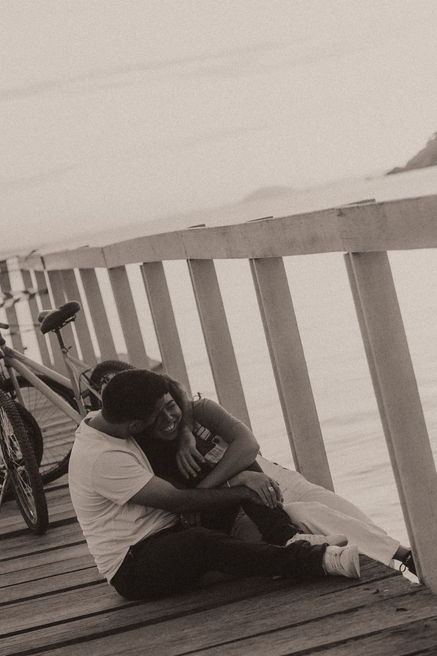 Artistic black and white photograph of people laying close together on wooden boardwalk slats showing intimacy and connection.