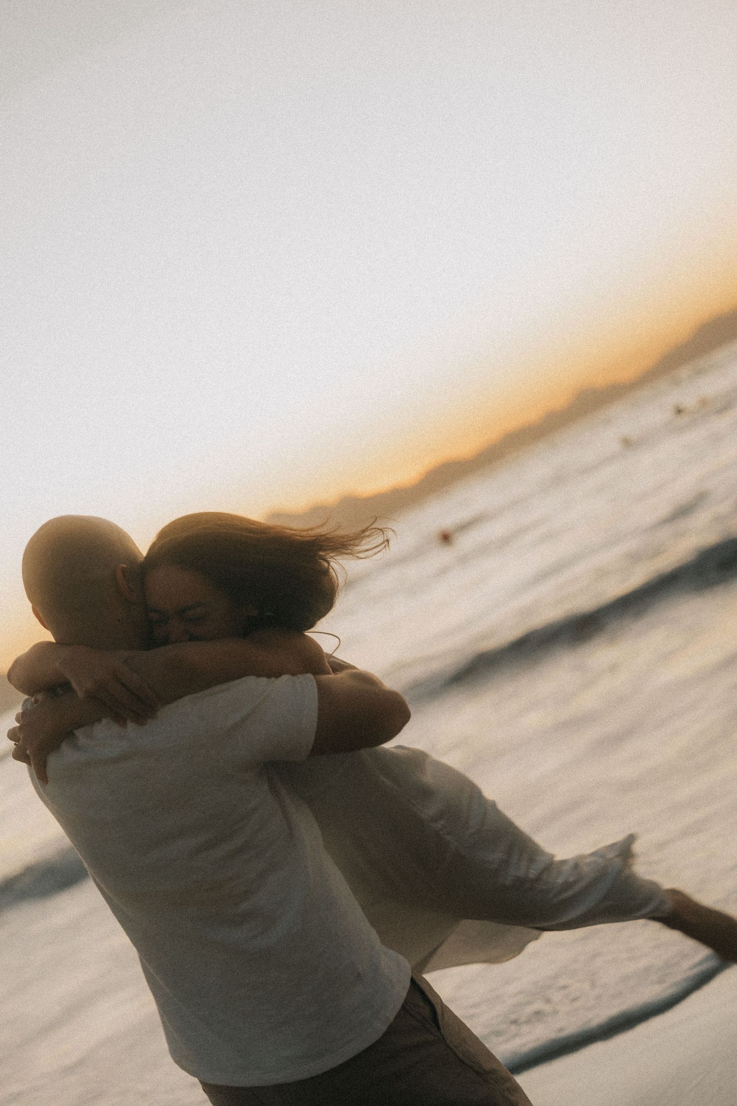 A couple embraces in silhouette against a sunset sky and ocean backdrop, creating a romantic seaside moment.