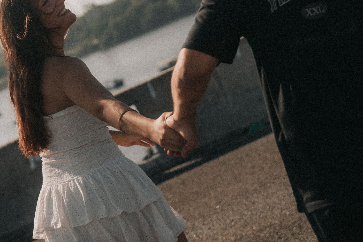 A couple holds hands at sunset in an intimate engagement or wedding photoshoot by a shoreline.