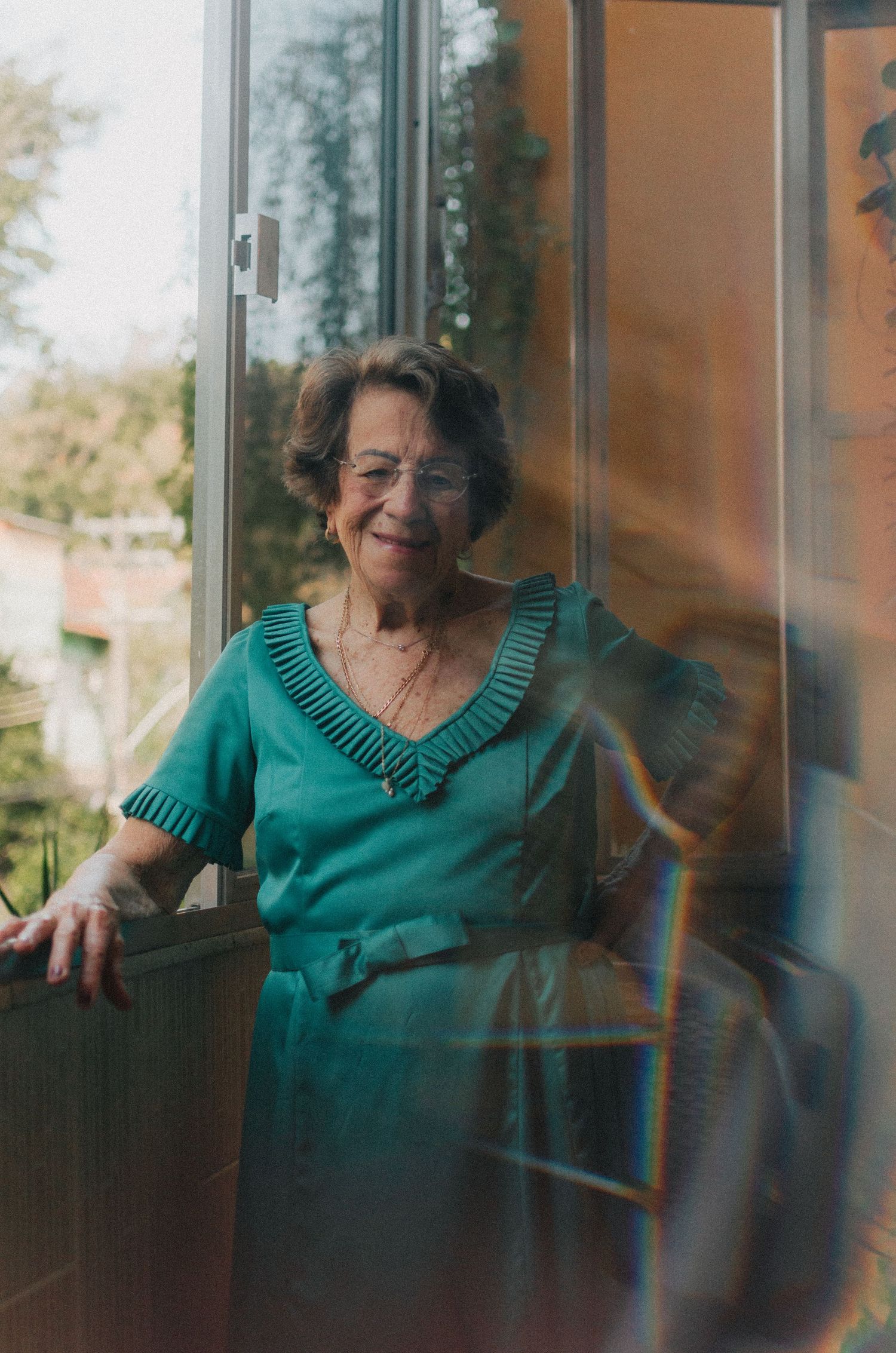 Person in teal dress smiling while sitting near a window with natural lighting.