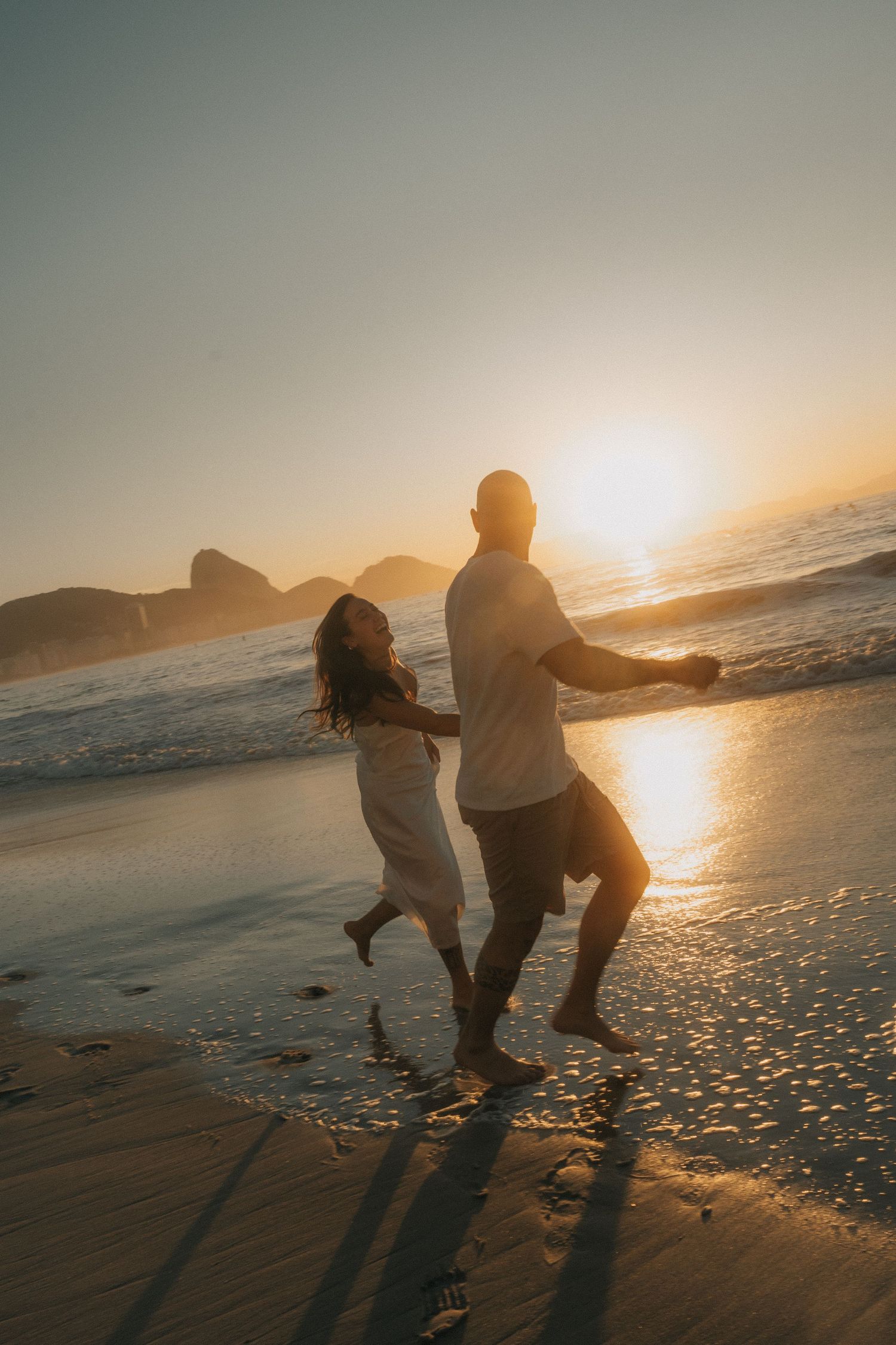 Silhouettes of people running and playing together on a beach at golden sunset casting long shadows across the sand.