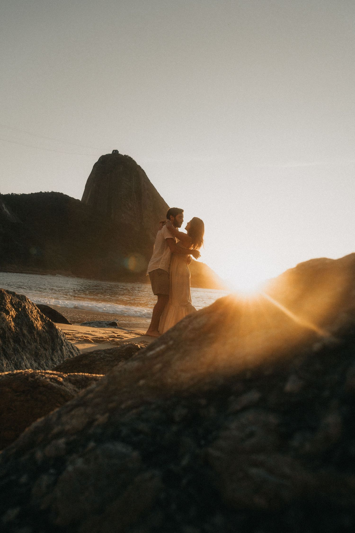 Romantic silhouette on rocky beach at sunset with Sugarloaf Mountain in Rio de Janeiro, Brazil in background.