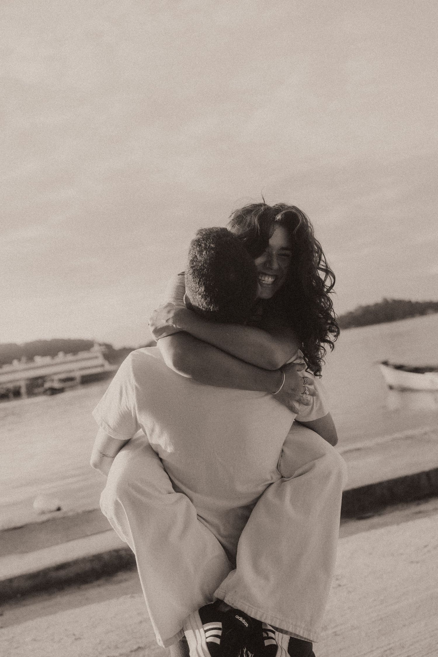 Two people in warm white sweaters embrace each other on a foggy beach in a black and white photograph.