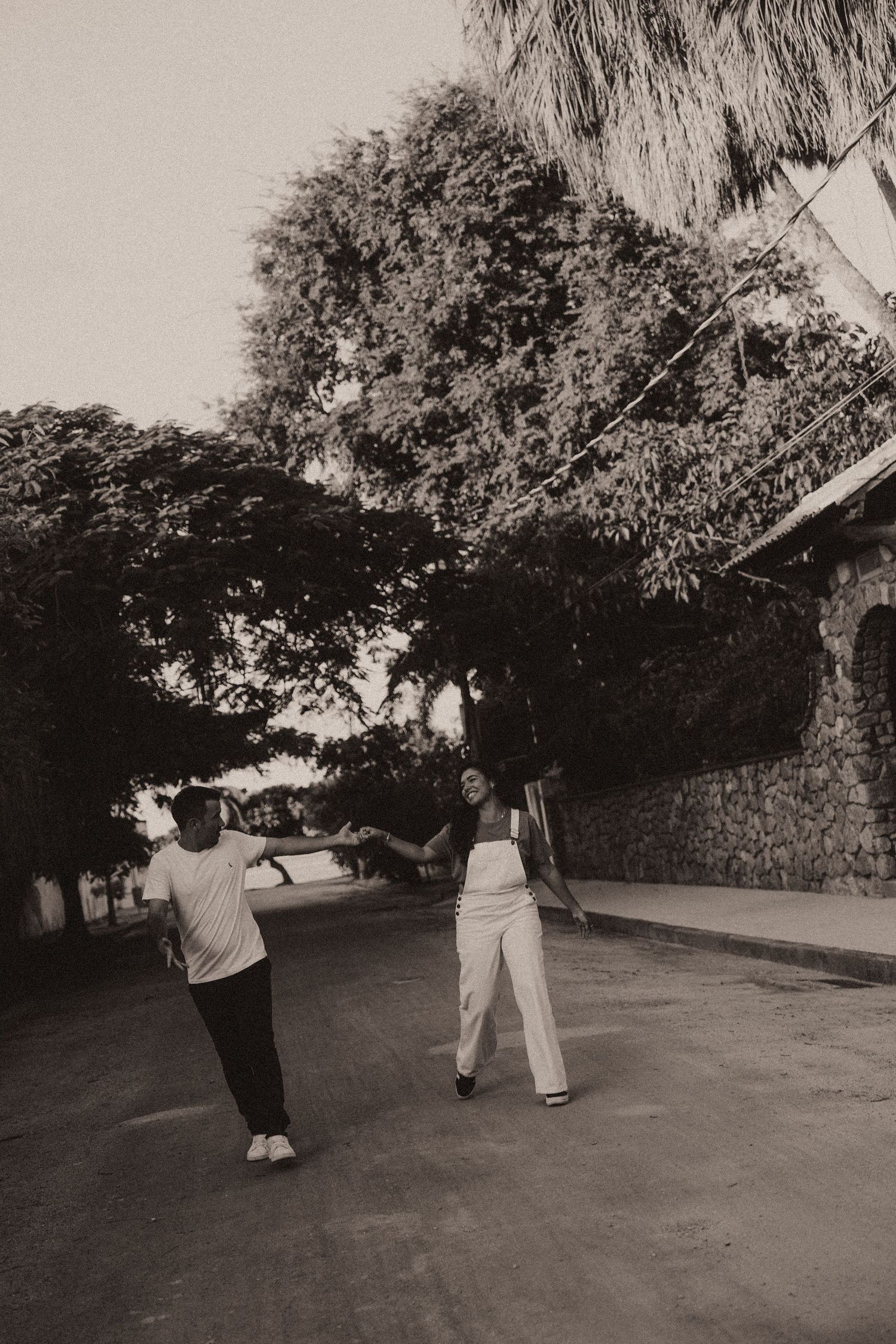 Two people walking outdoors in casual clothing along a path surrounded by trees in black and white photography.