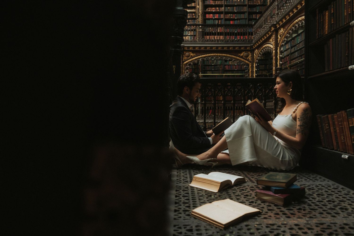 A person sits at a wooden desk in a dimly lit library with antique books and ornate architectural details surrounding them.