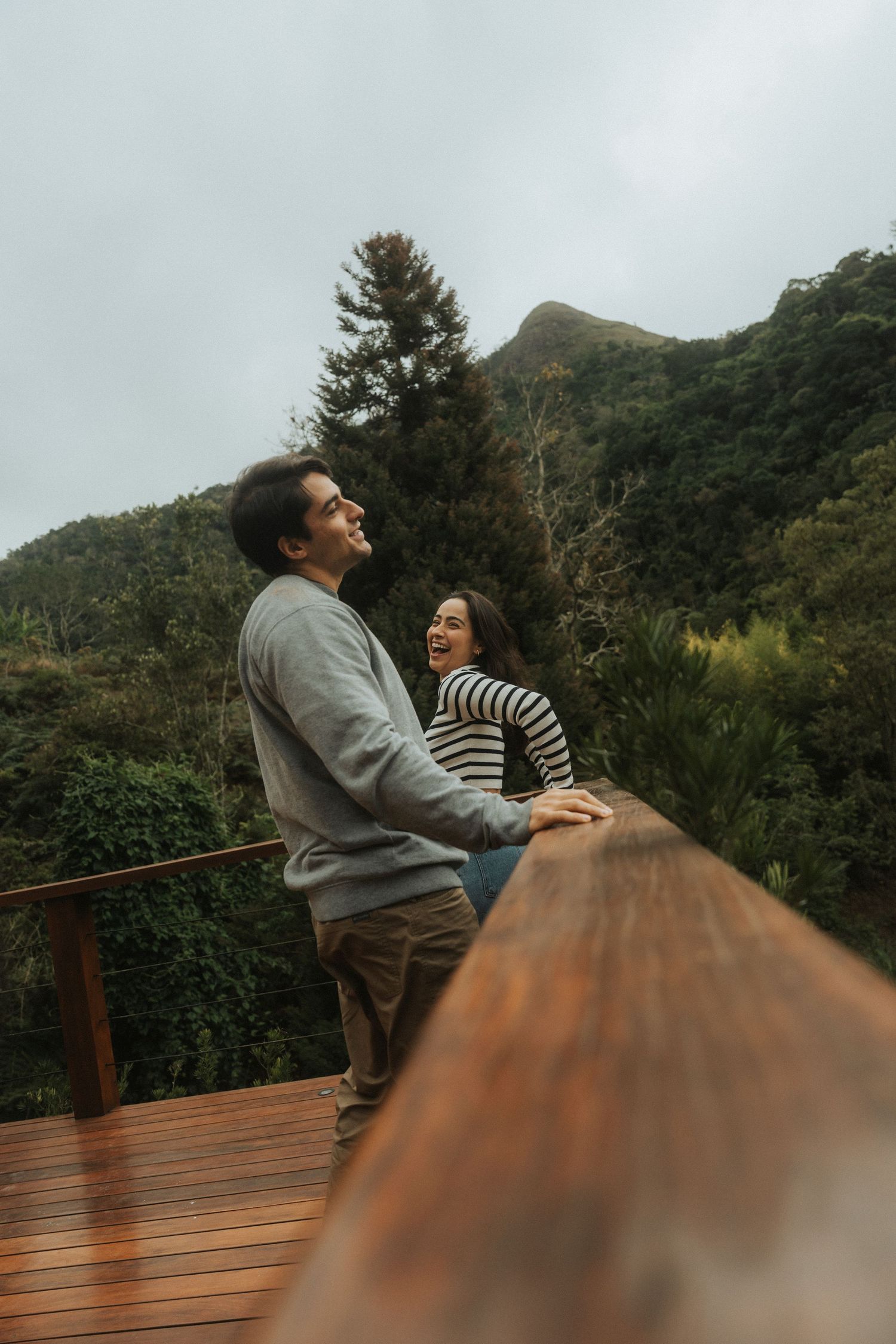 A couple shares a joyful moment together on a wooden deck overlooking lush mountain scenery on a misty day.