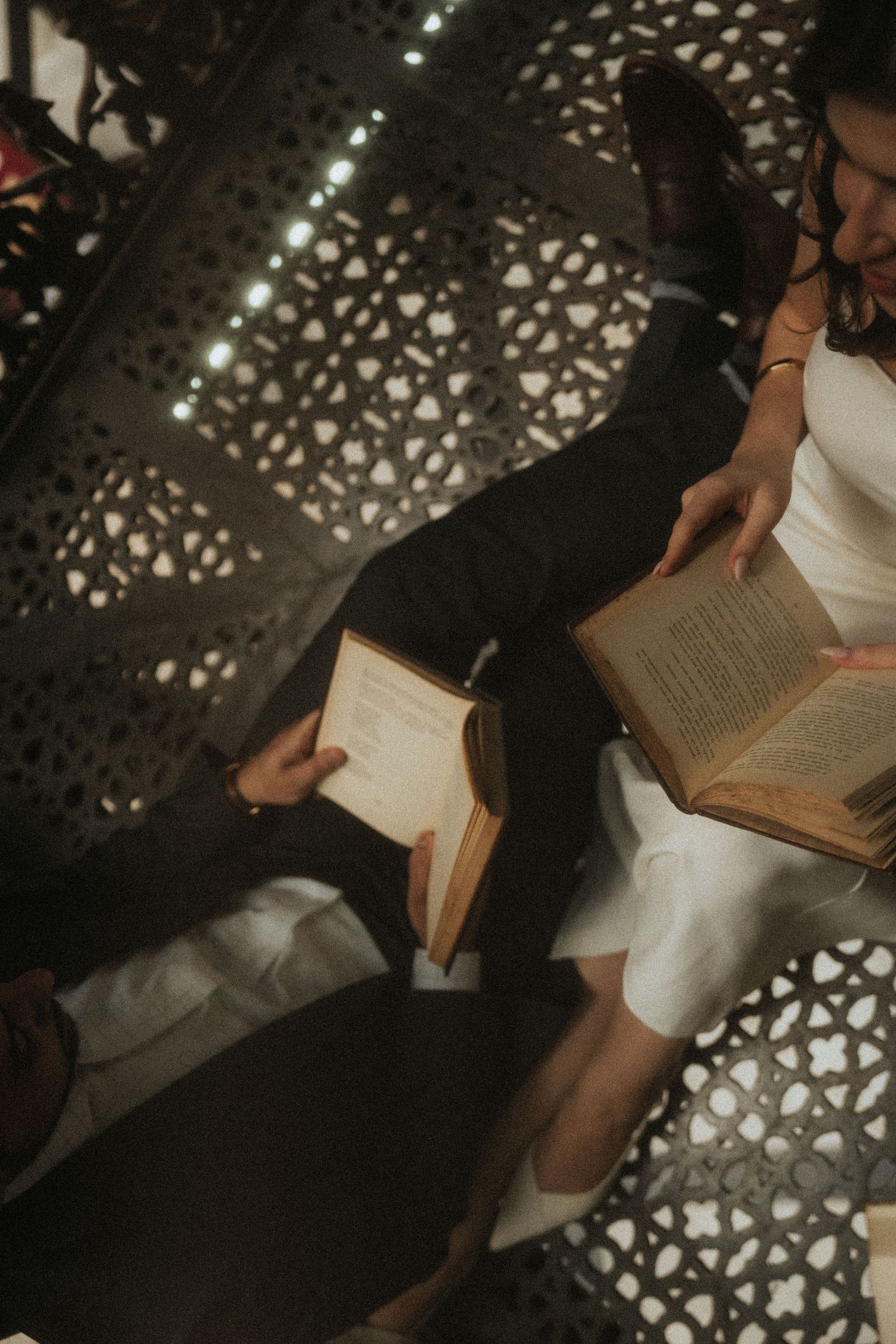 Person in white dress reading books on floor with decorative shadow patterns cast from above.