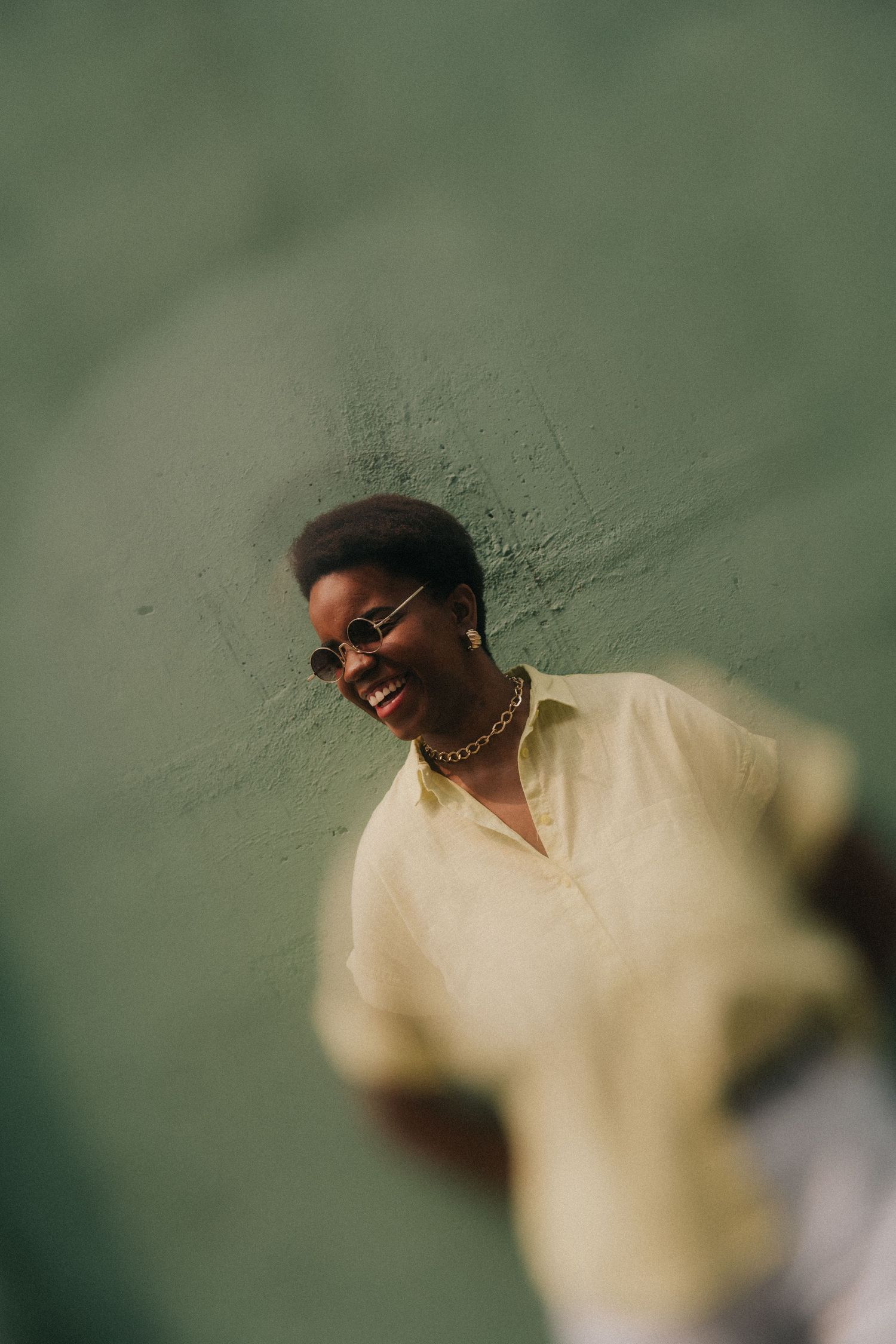A sequence of blurred shots showing someone in a light yellow shirt with sunglasses smiling against a green background.