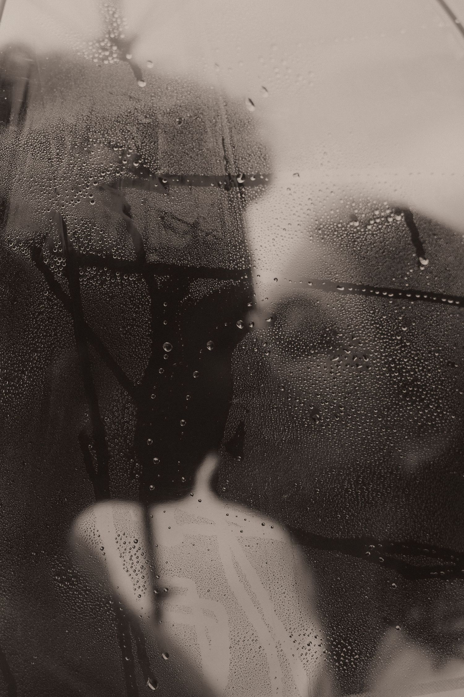 Water droplets on a foggy glass window create a moody, atmospheric scene in black and white photography.