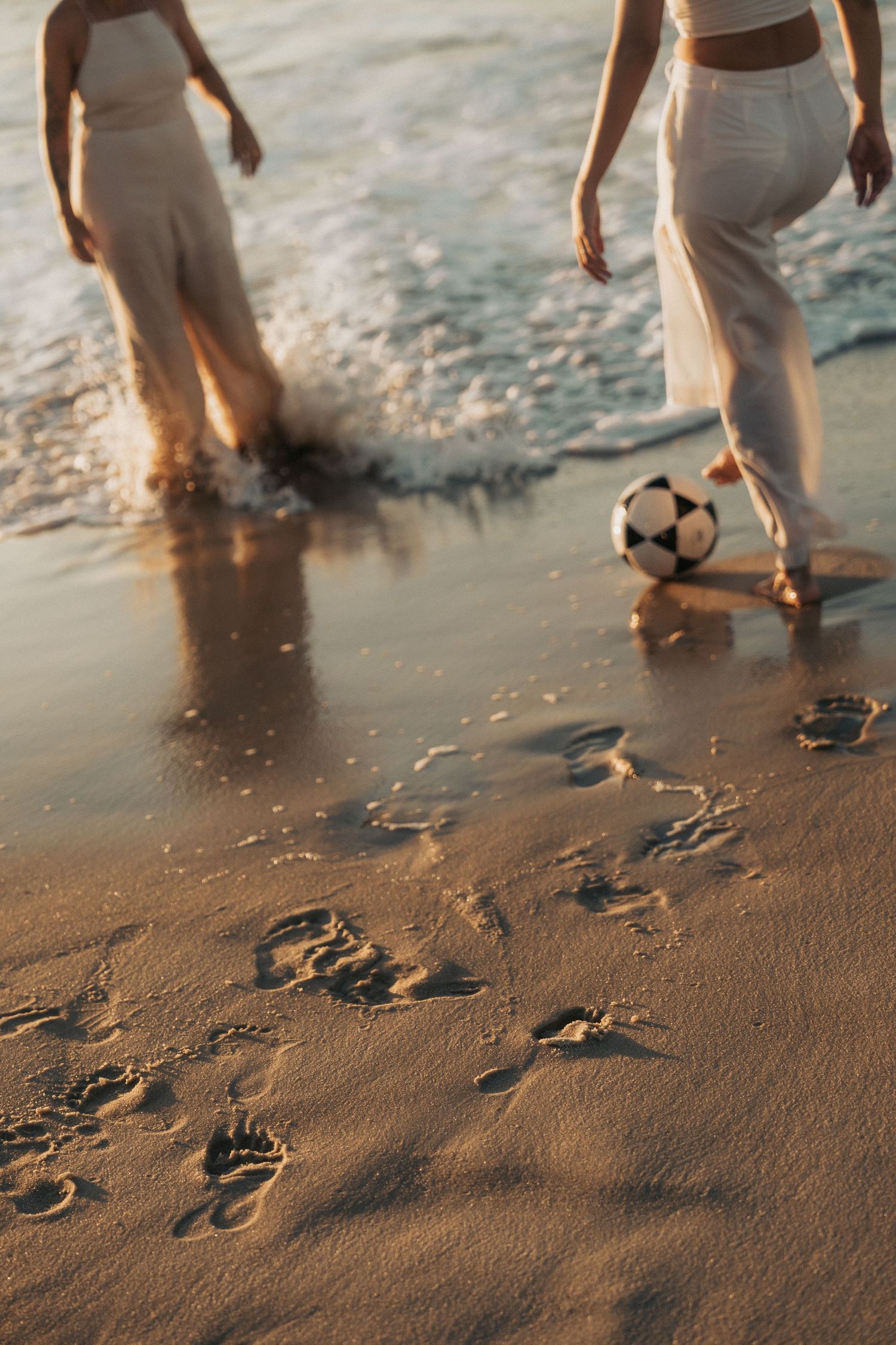 Multiple frames showing footprints being made in wet beach sand as waves wash over feet playing with a soccer ball.
