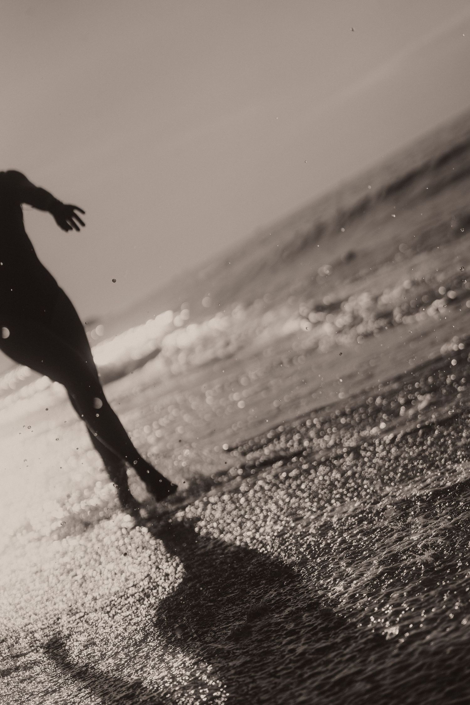 Black and white series of footsteps walking across a sandy beach, creating dramatic shadows in the sunlight.