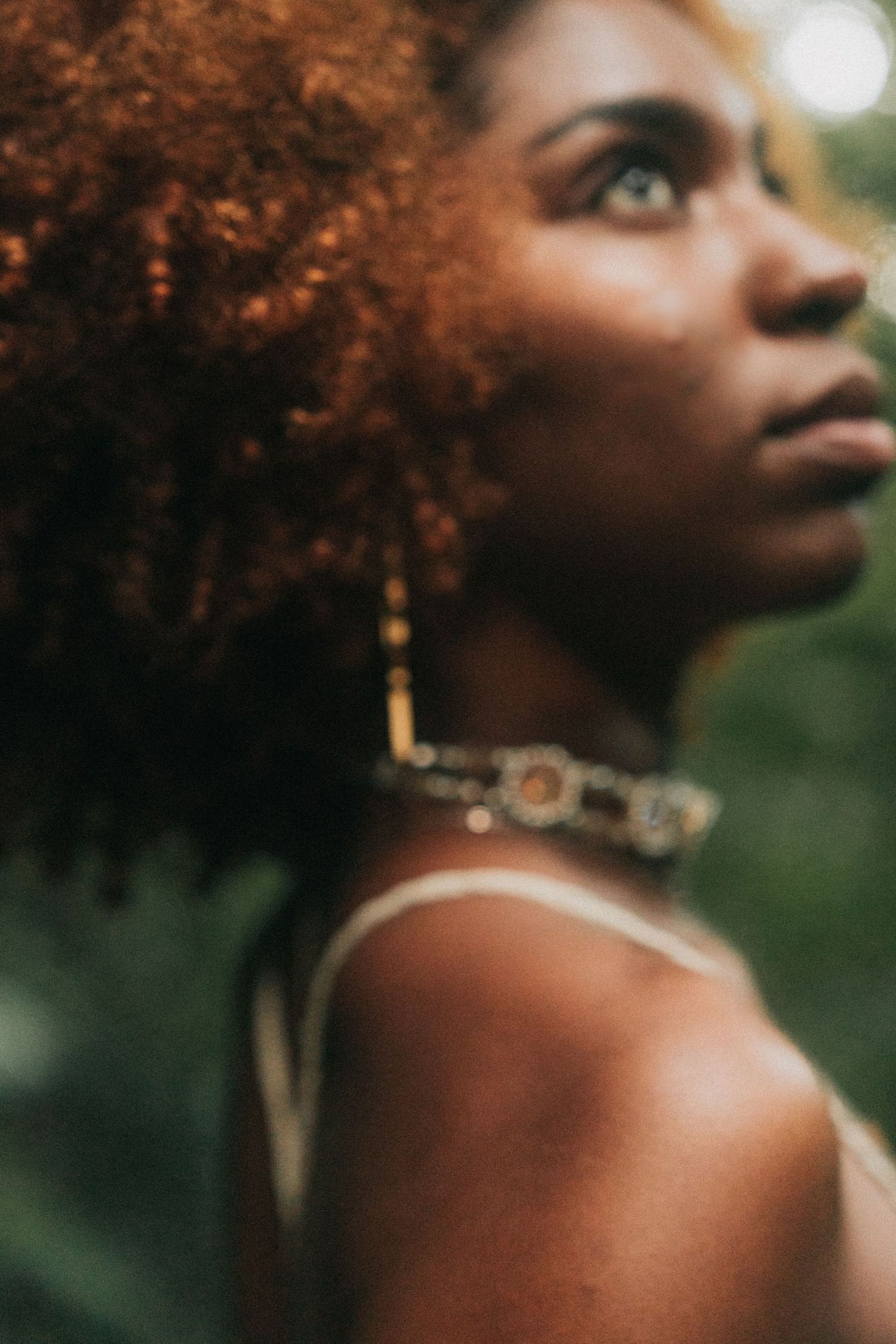 Side profile portraits showcase natural curly red hair and golden jewelry against a soft outdoor backdrop.