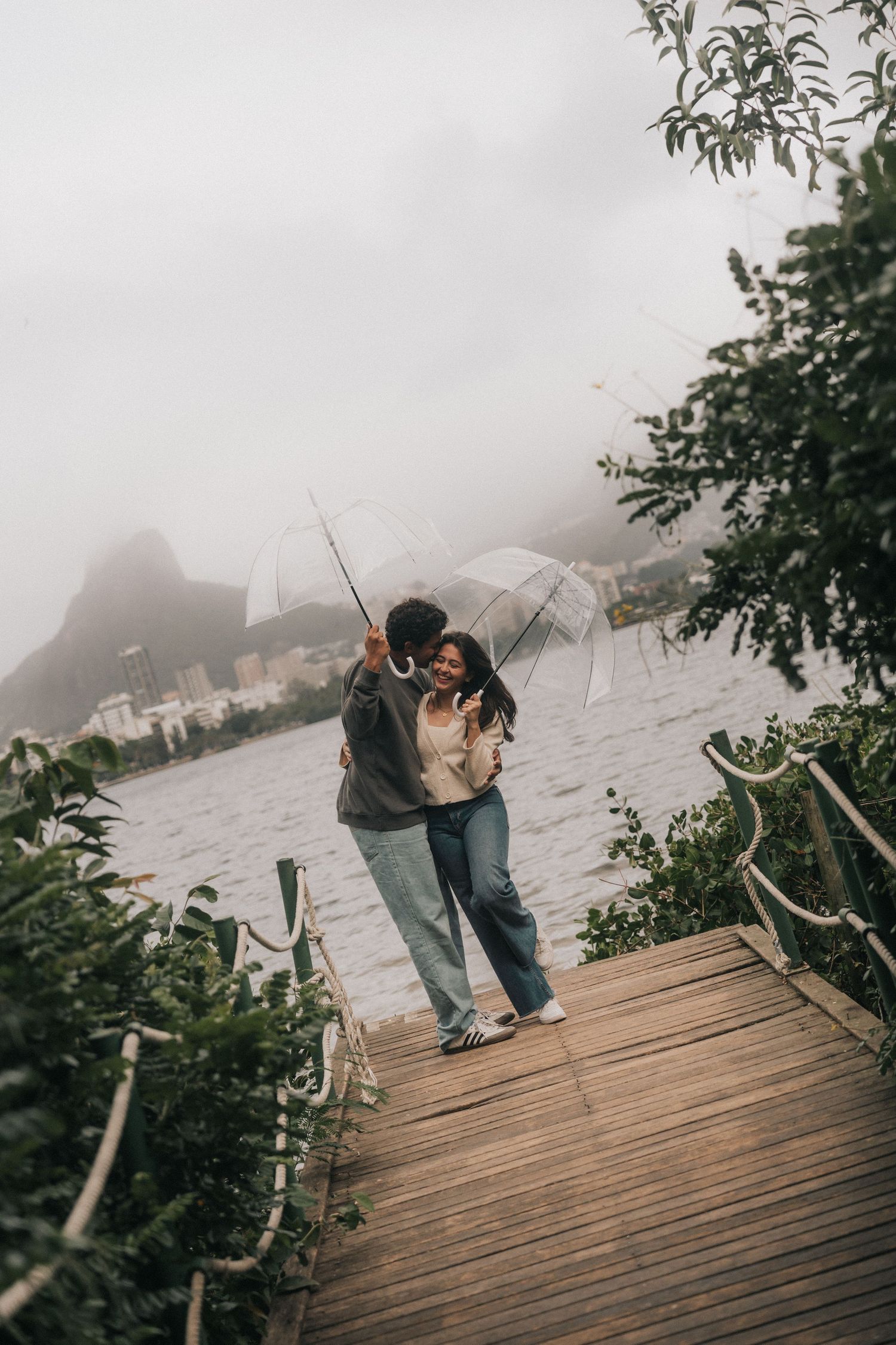 A person in casual attire fishing from a wooden dock on a misty morning by a lake.