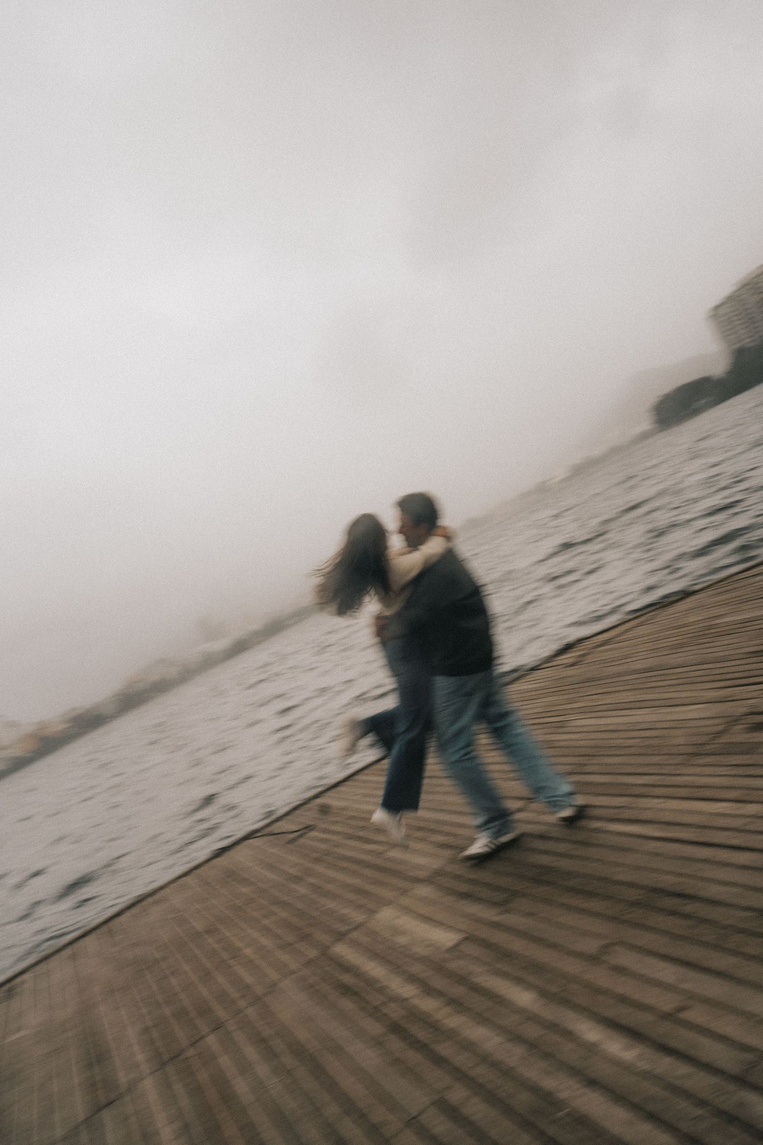 Blurry motion sequence showing a person walking down a wooden boardwalk by a misty ocean shore.