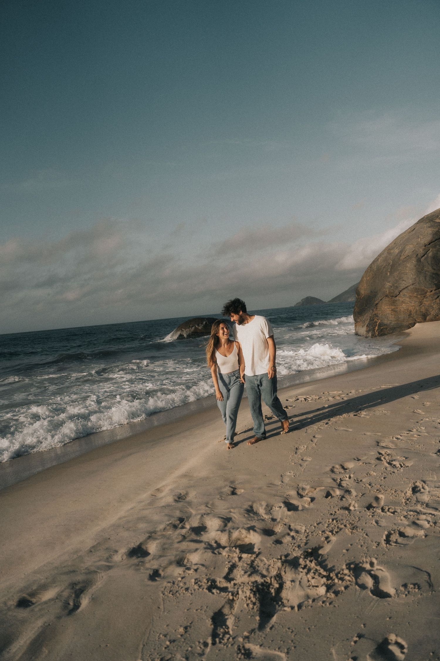 Moody seaside photography sequence showing couple walking and exploring rocky beach with dramatic coastal cliffs at sunset.