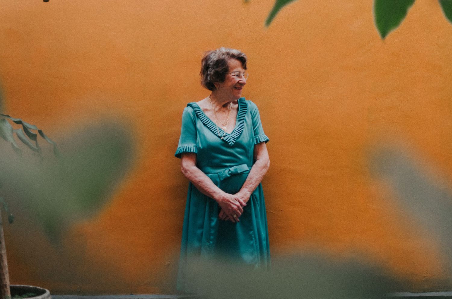 Woman in turquoise dress poses gracefully against orange wall in outdoor portrait session.