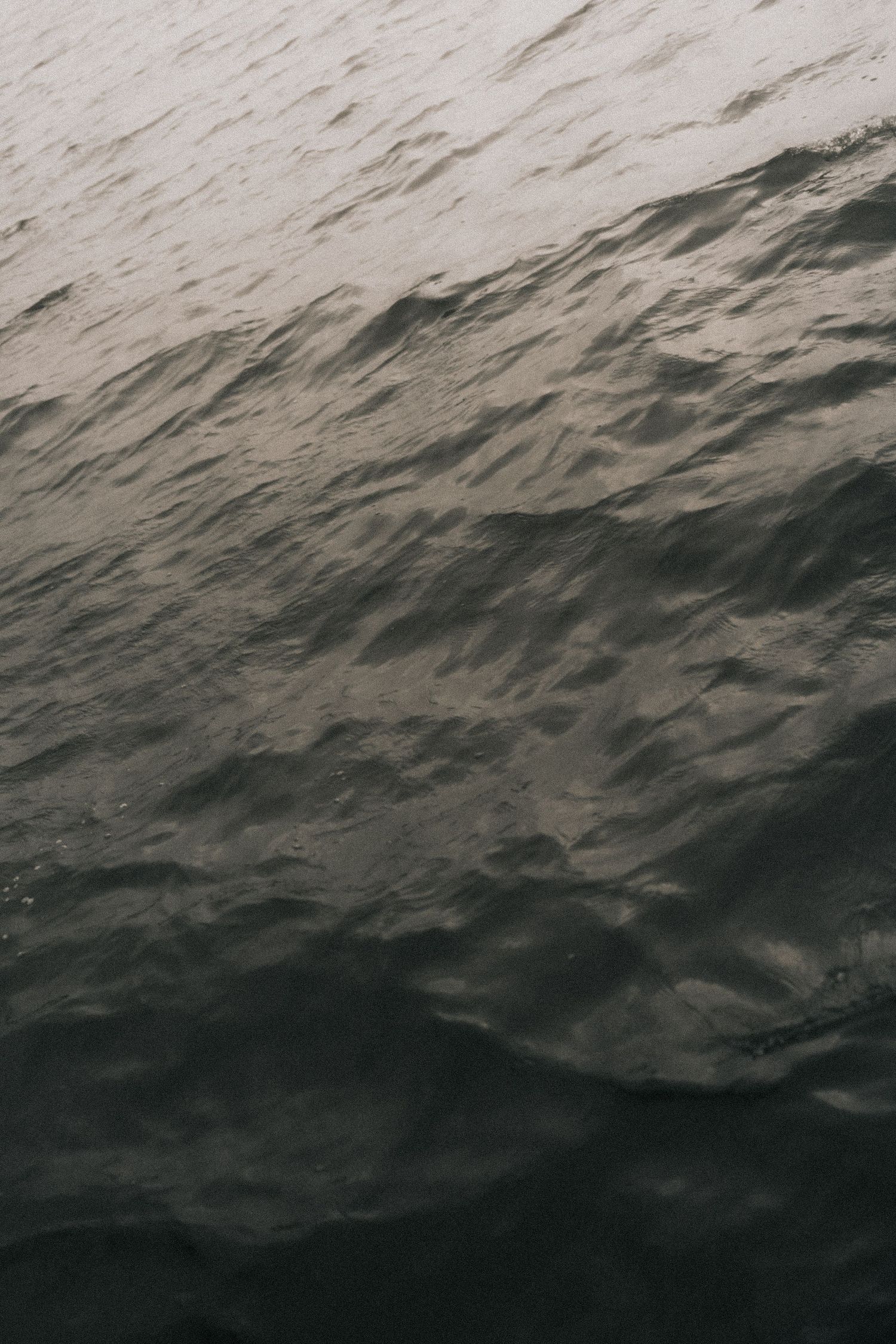 Dark, textured ocean waves create a moody seascape pattern under an overcast sky.