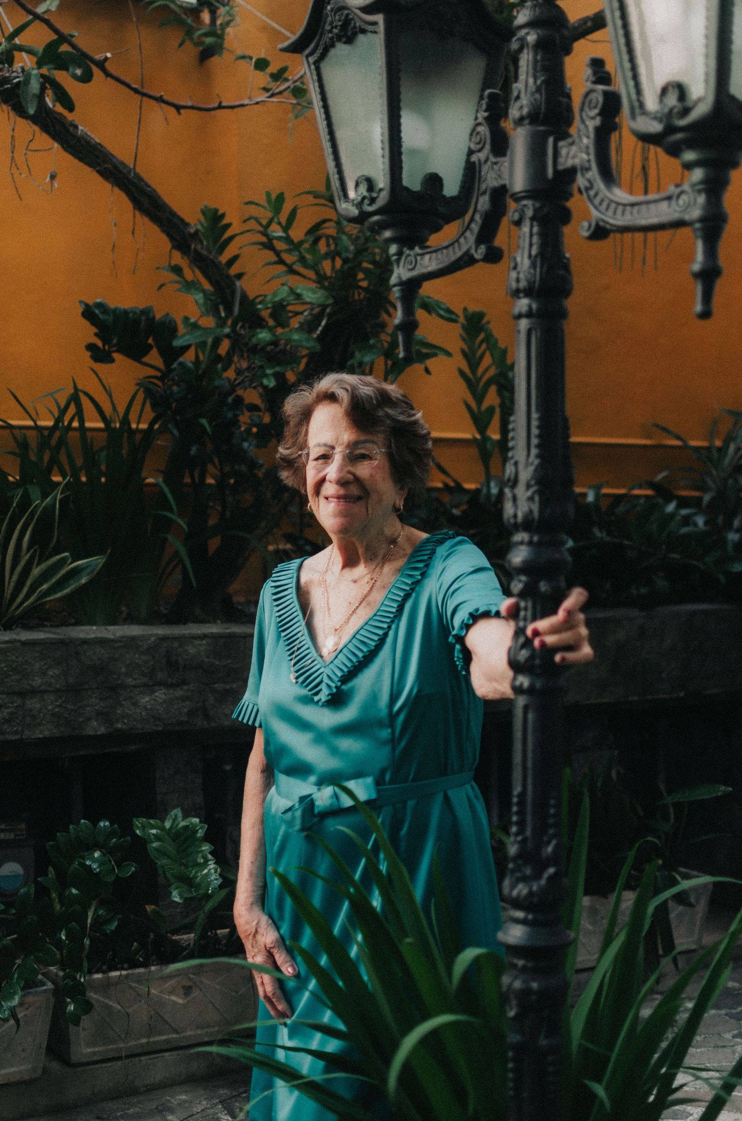 Four sequential photos show someone in a turquoise dress posing playfully near a tropical plant against an orange wall.