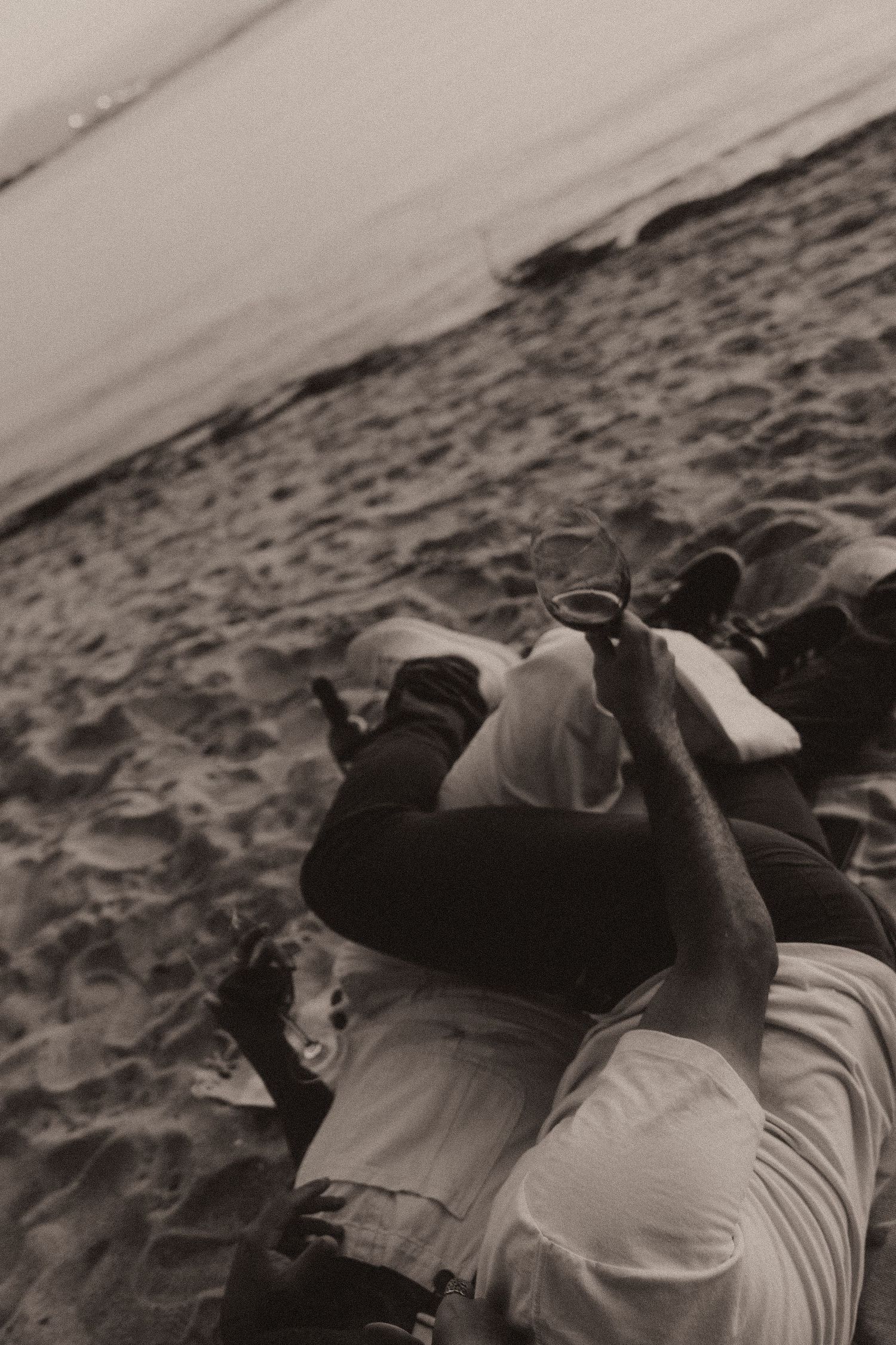 Two figures lie in an intimate embrace on a sandy beach in a black and white artistic composition.