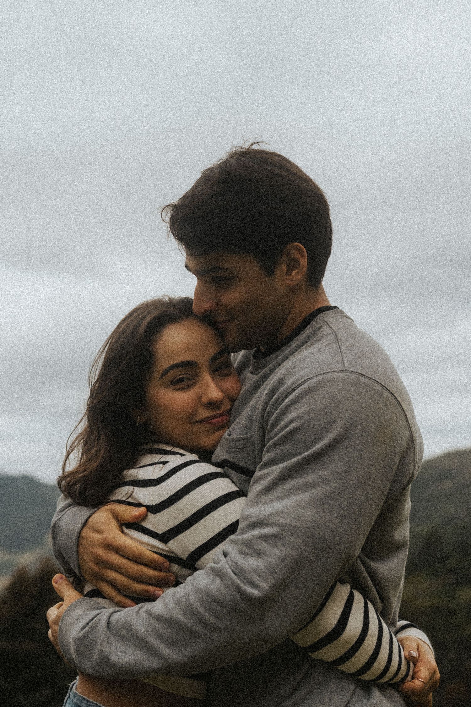 A couple in a romantic embrace wearing casual clothing share tender moments in a series of moody outdoor photos.