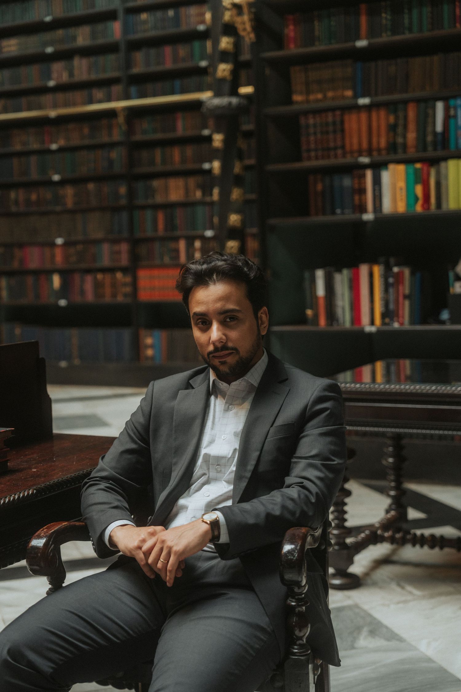 Professional portrait session in a library with dark wood bookshelves and elegant antique furniture.