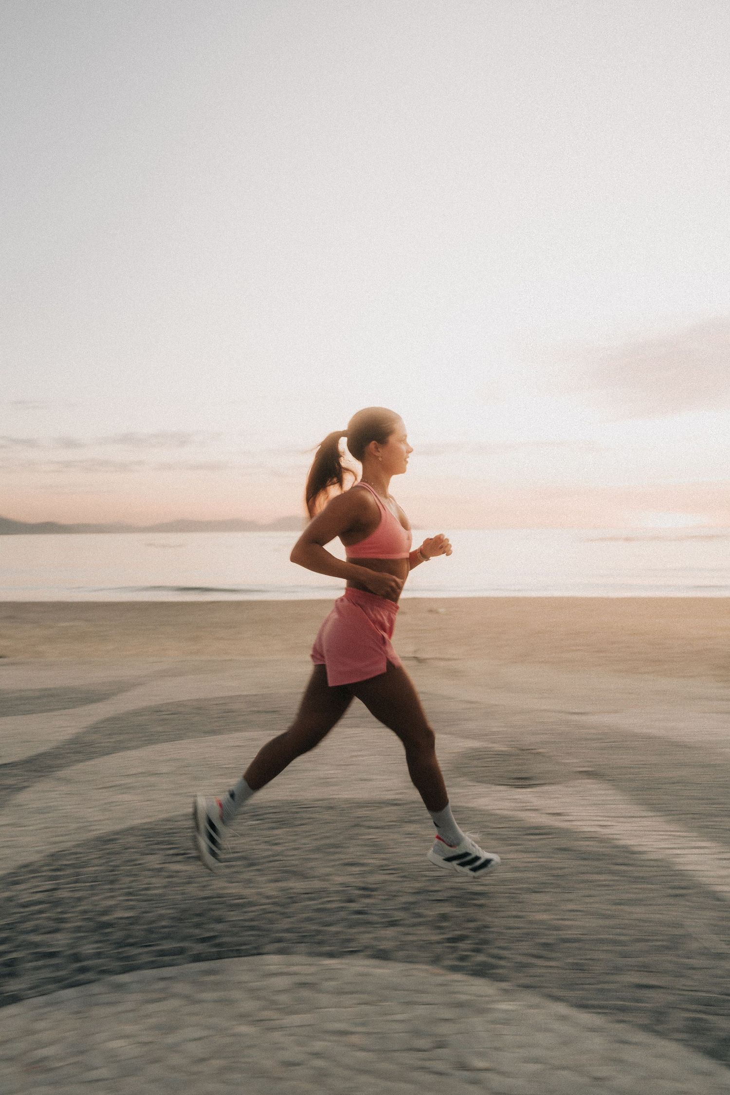 A person in athletic wear leaps and jumps across a sandy beach during sunset, creating a dynamic motion sequence.