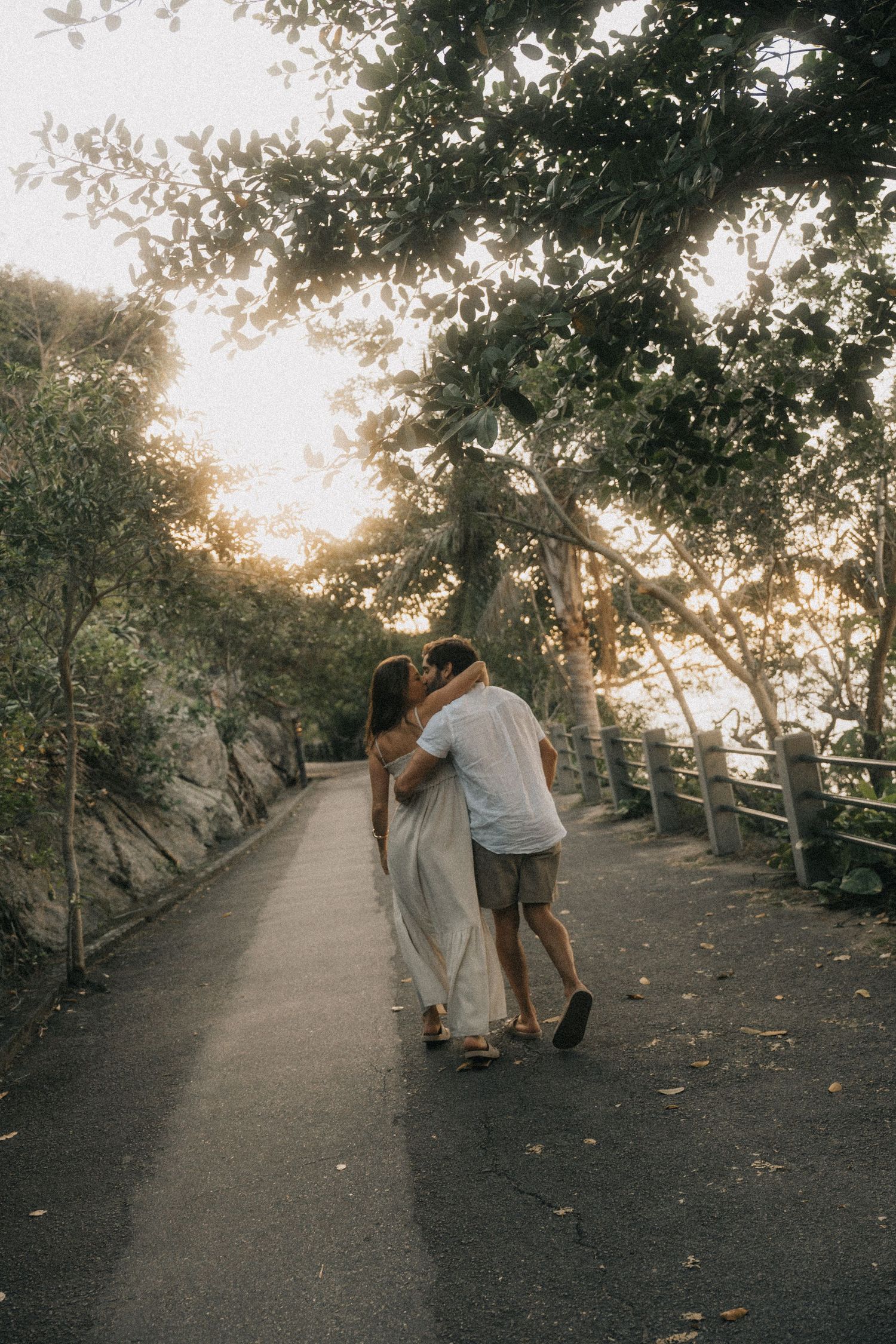 A couple embraces on a scenic tree-lined pathway at sunset creating a romantic silhouette against the golden light.