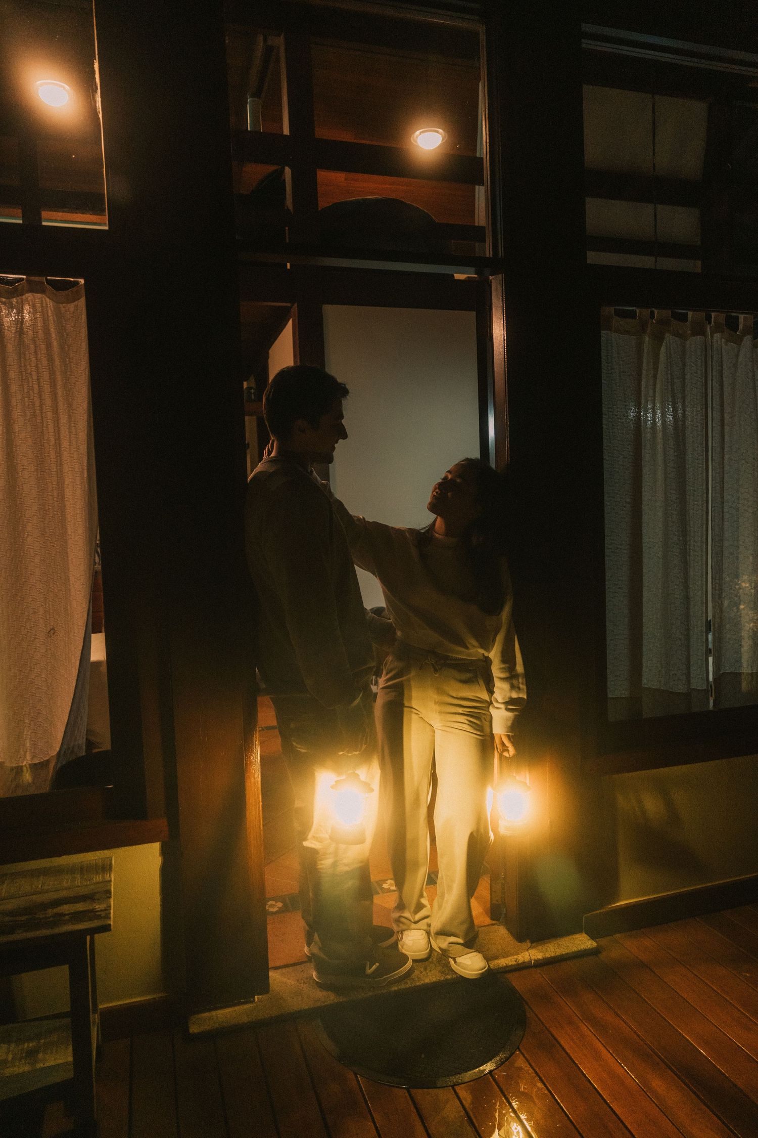 Person holding a lantern illuminates a dark wooden hallway with warm glowing light at night.