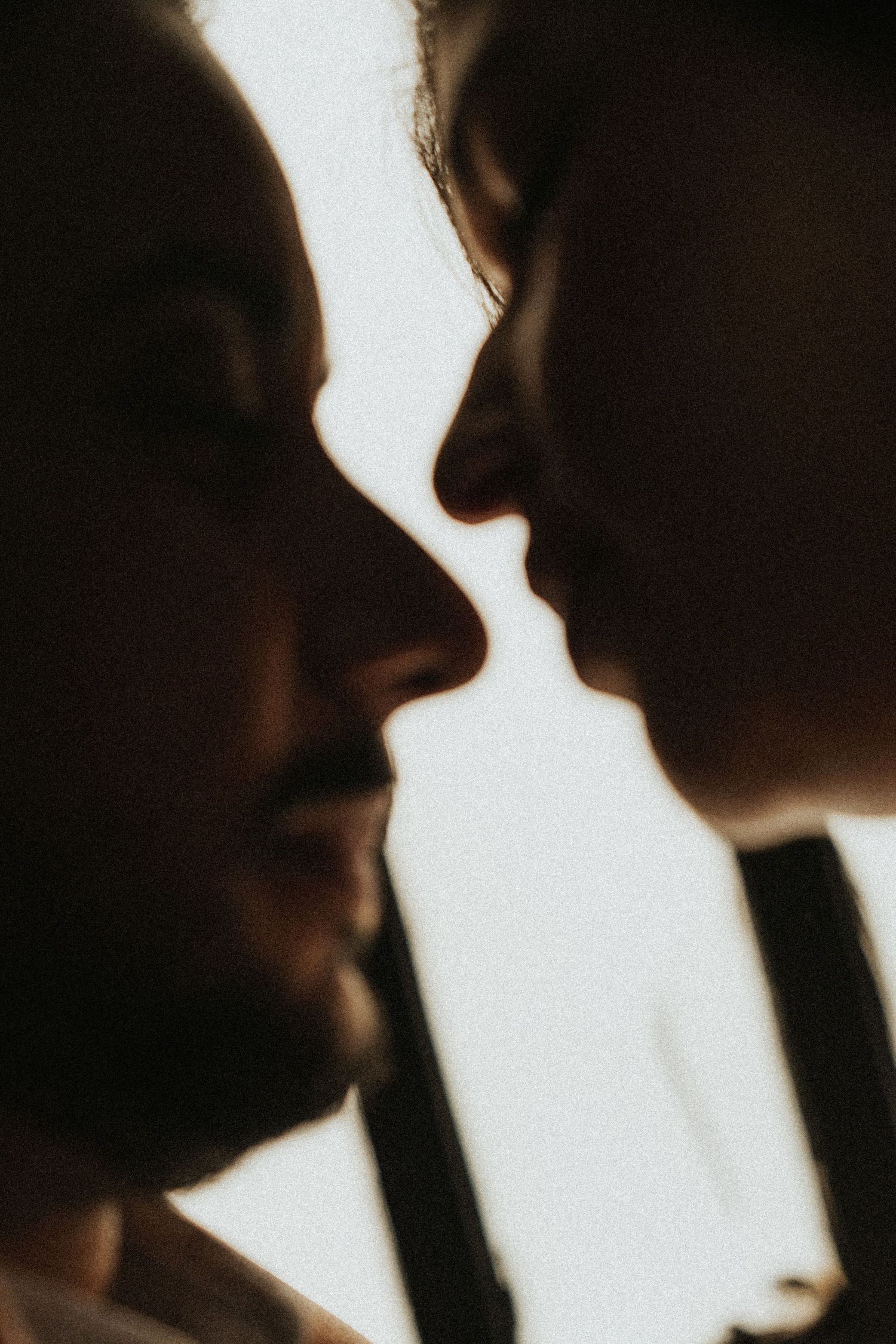 Silhouetted profiles of two people in close proximity against a light background, creating a romantic shadow effect.