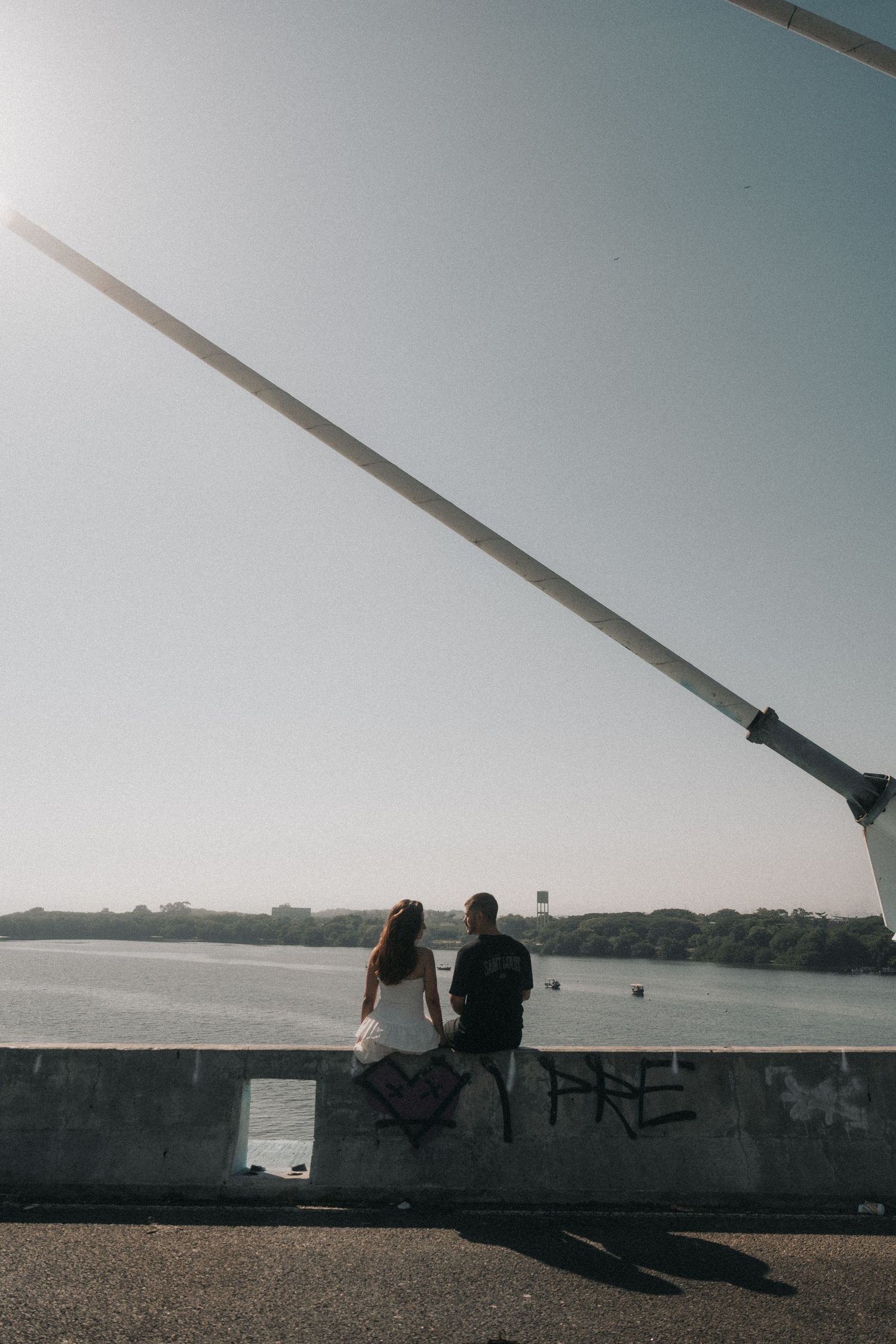 Two silhouetted figures sit on a wall overlooking a serene waterfront view at dusk.