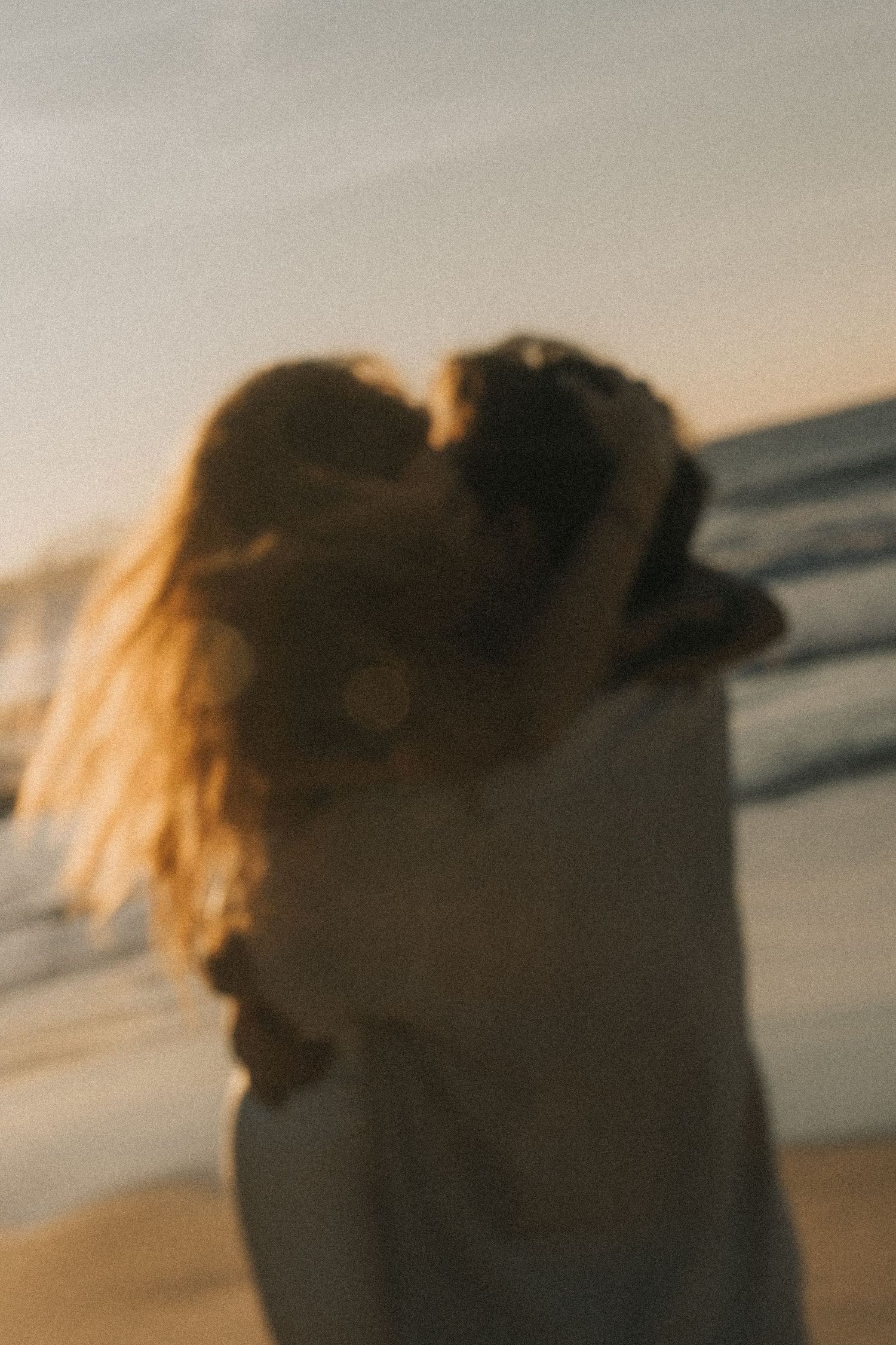 A blurred silhouette with flowing hair against a warm sunset sky on a beach.