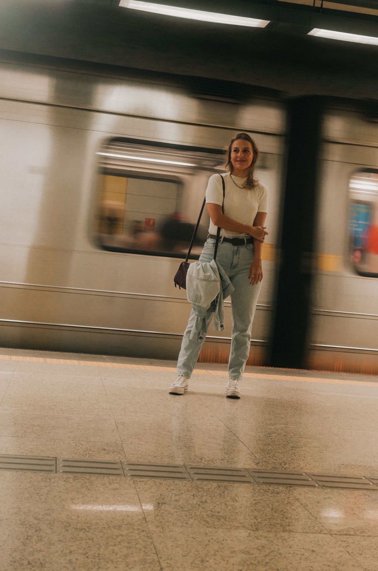 Motion blurred subway train passing by while person waits on platform in New York underground station.