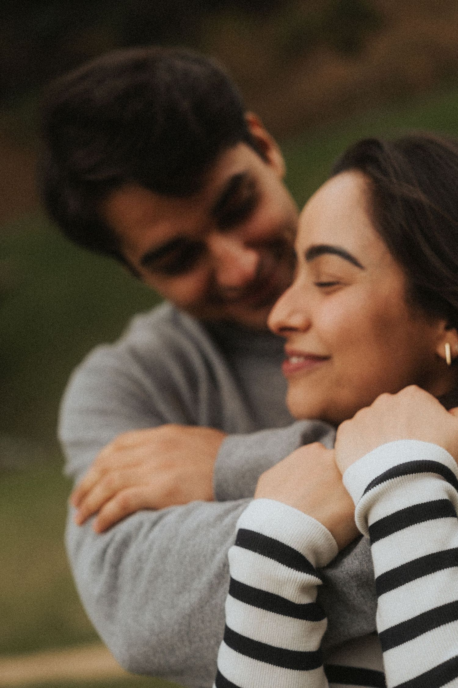A couple shares an intimate moment outdoors while wearing a gray sweater and striped sleeves.