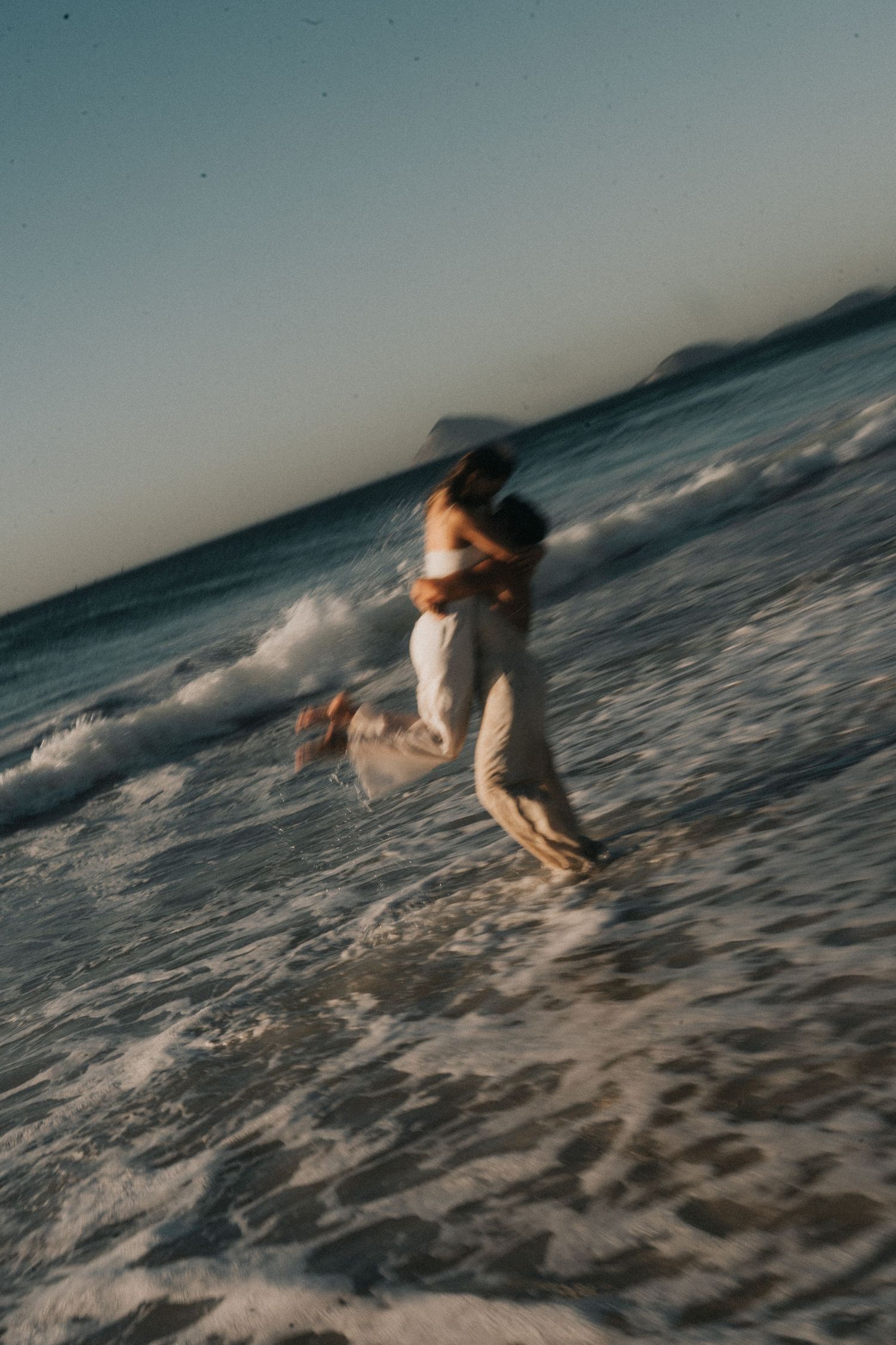 A sequence of photos showing someone in a white dress running and splashing through ocean waves at dusk.