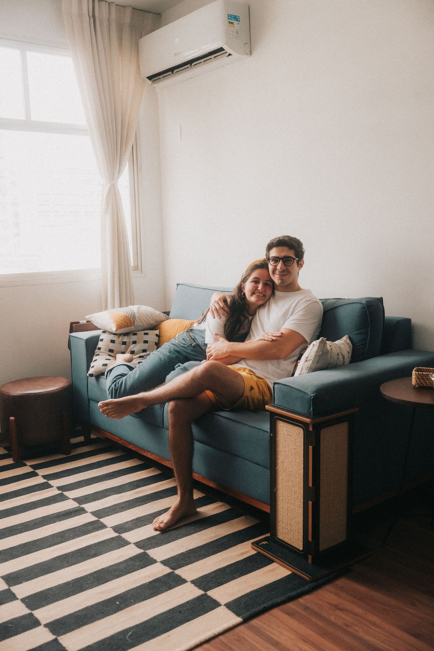 Person lounging across blue sofa in modern living room with striped rug and hardwood floors.