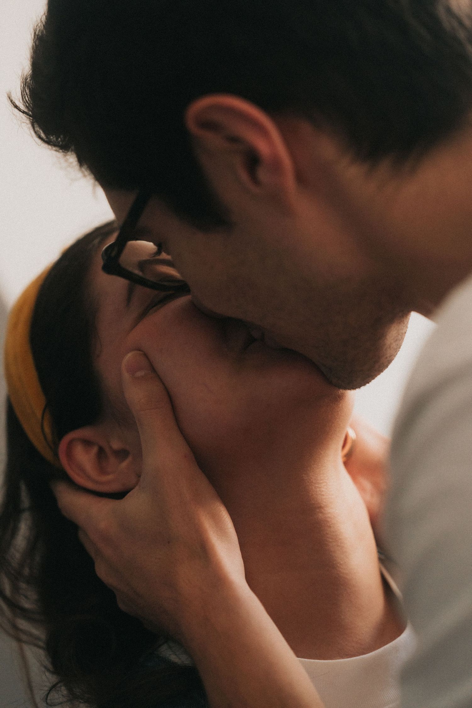 Romantic couple in an intimate kiss with dramatic side lighting creating a tender emotional moment.