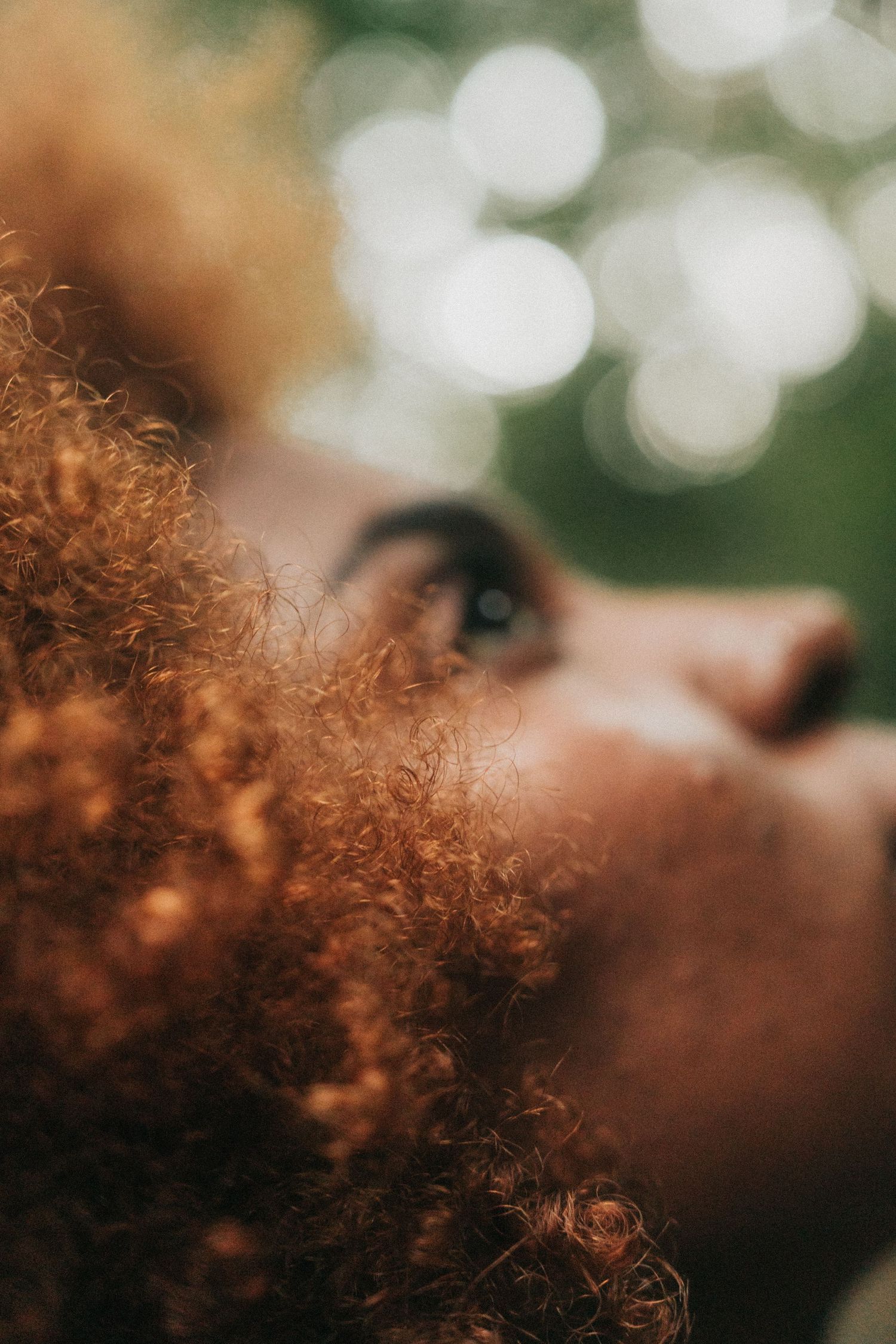 Close-up artistic portrait showing curly ginger hair illuminated by soft bokeh lights in the background.