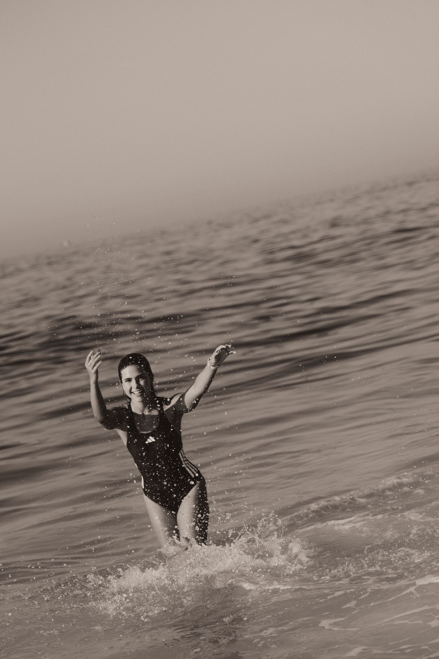 Black and white photo of someone swimming and splashing playfully in the rippling ocean waters.