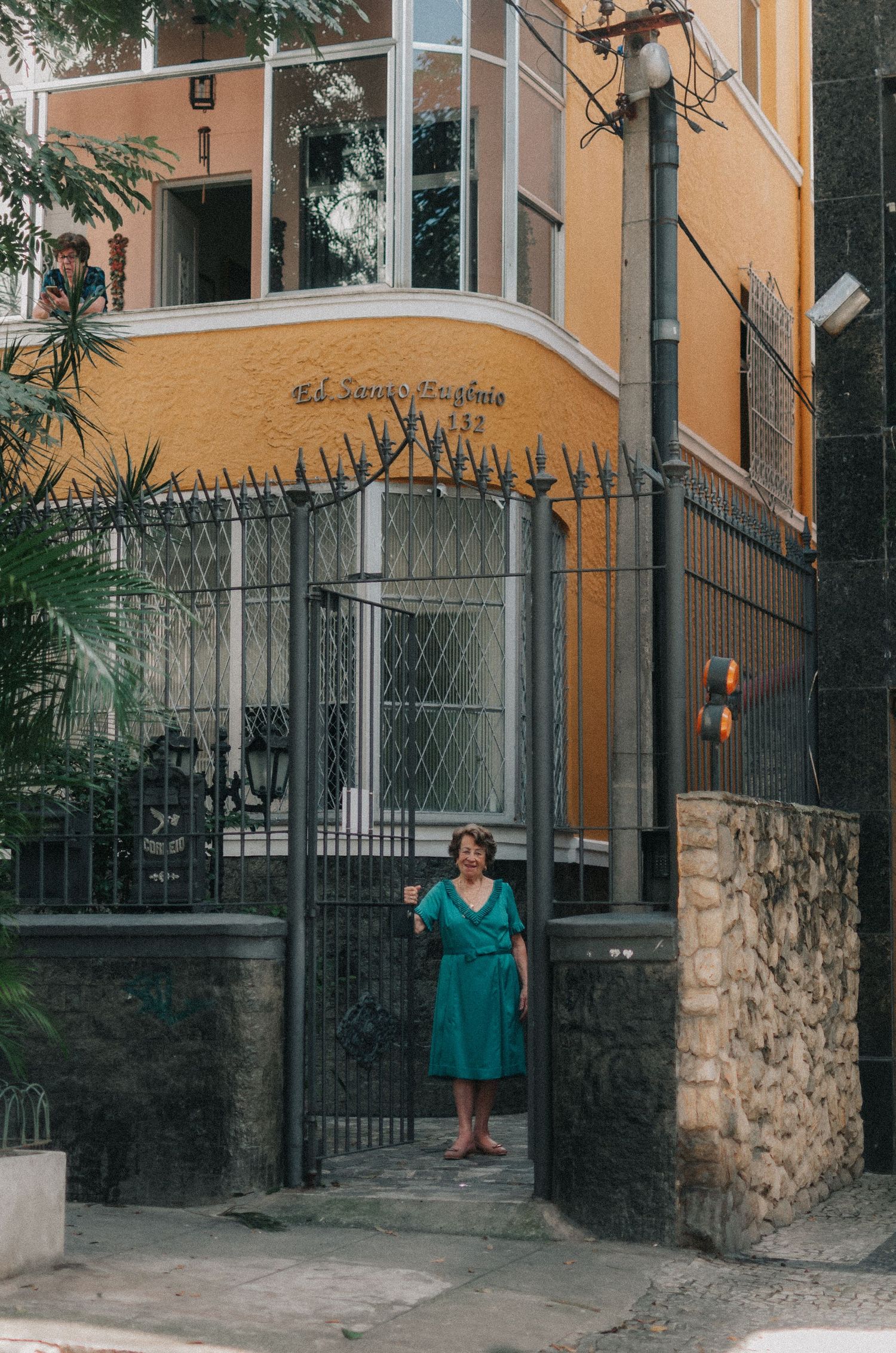 Multiple views of a person in a turquoise dress standing by a wrought iron gate entrance to a residential building.