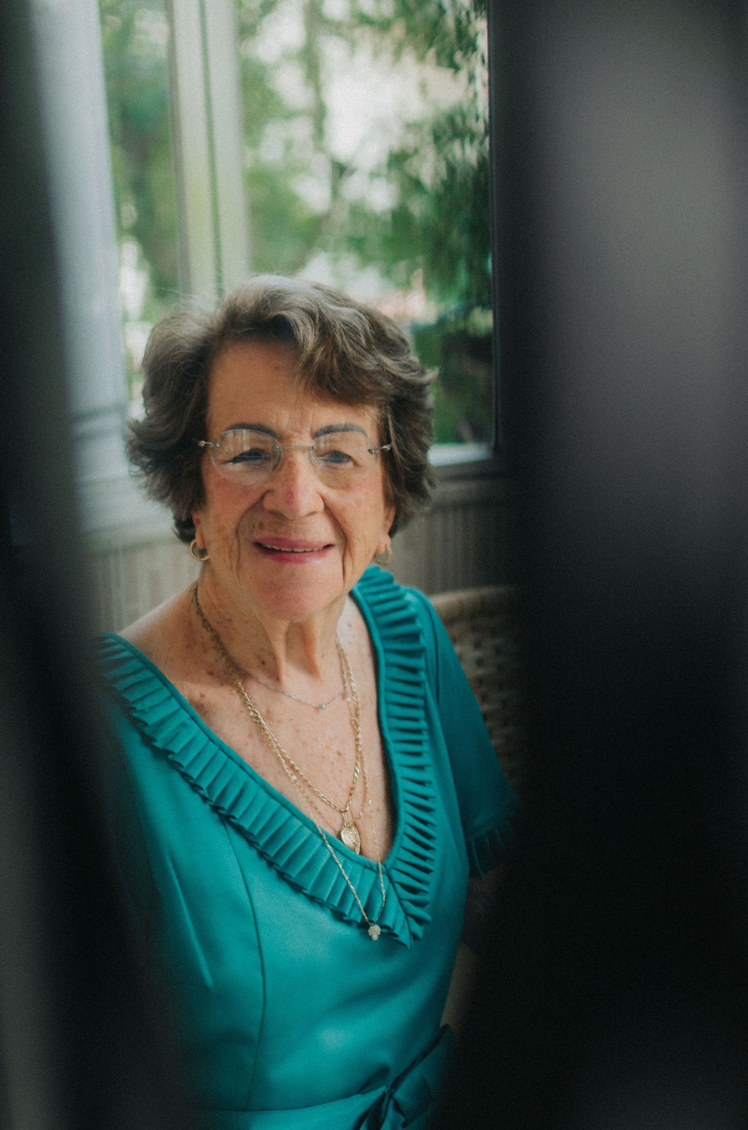 Triptych portrait in teal of an elderly woman wearing glasses and a necklace against a blurred background.