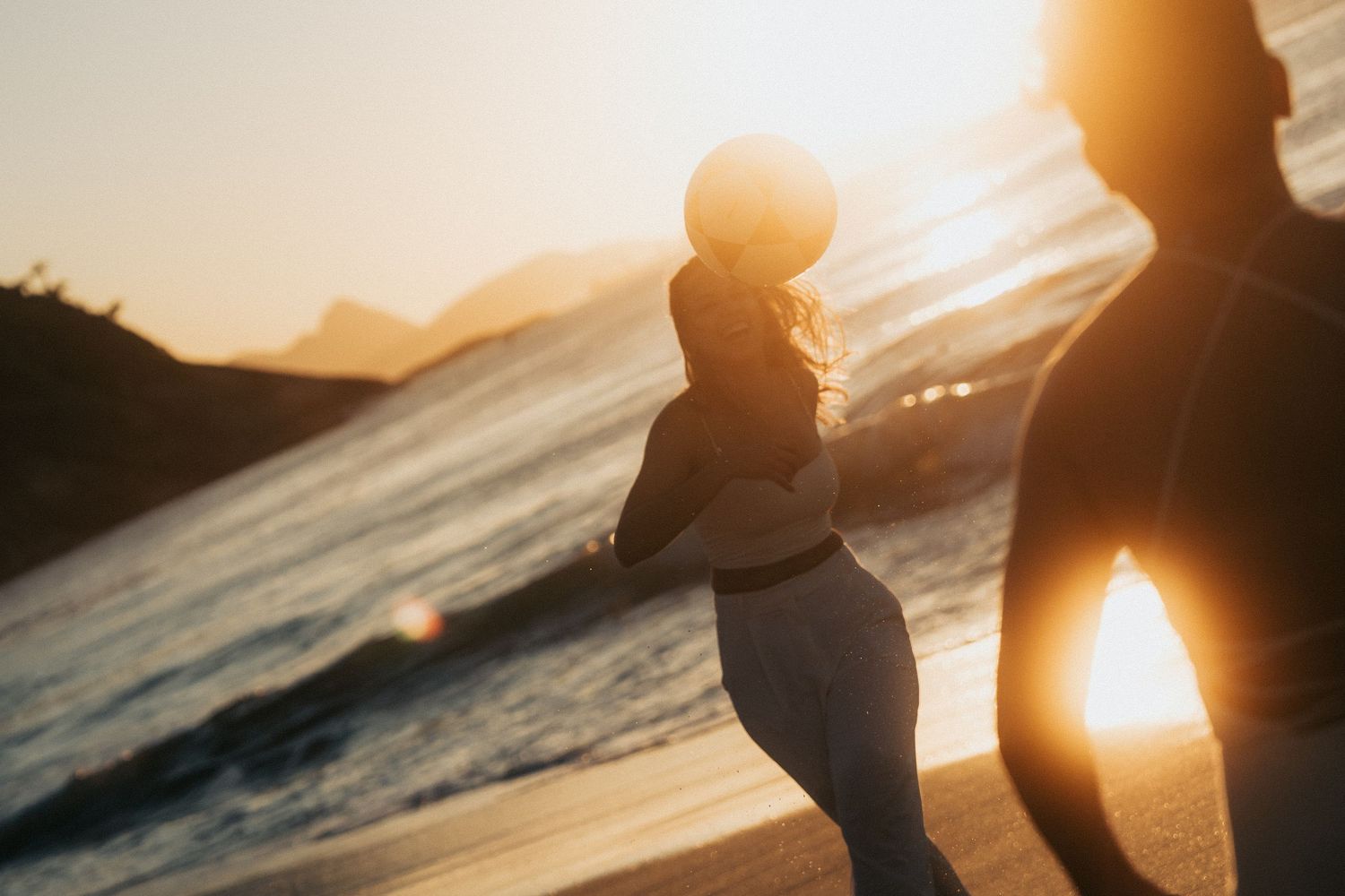 Dark silhouette of person standing on shoreline during golden sunset over ocean waves.