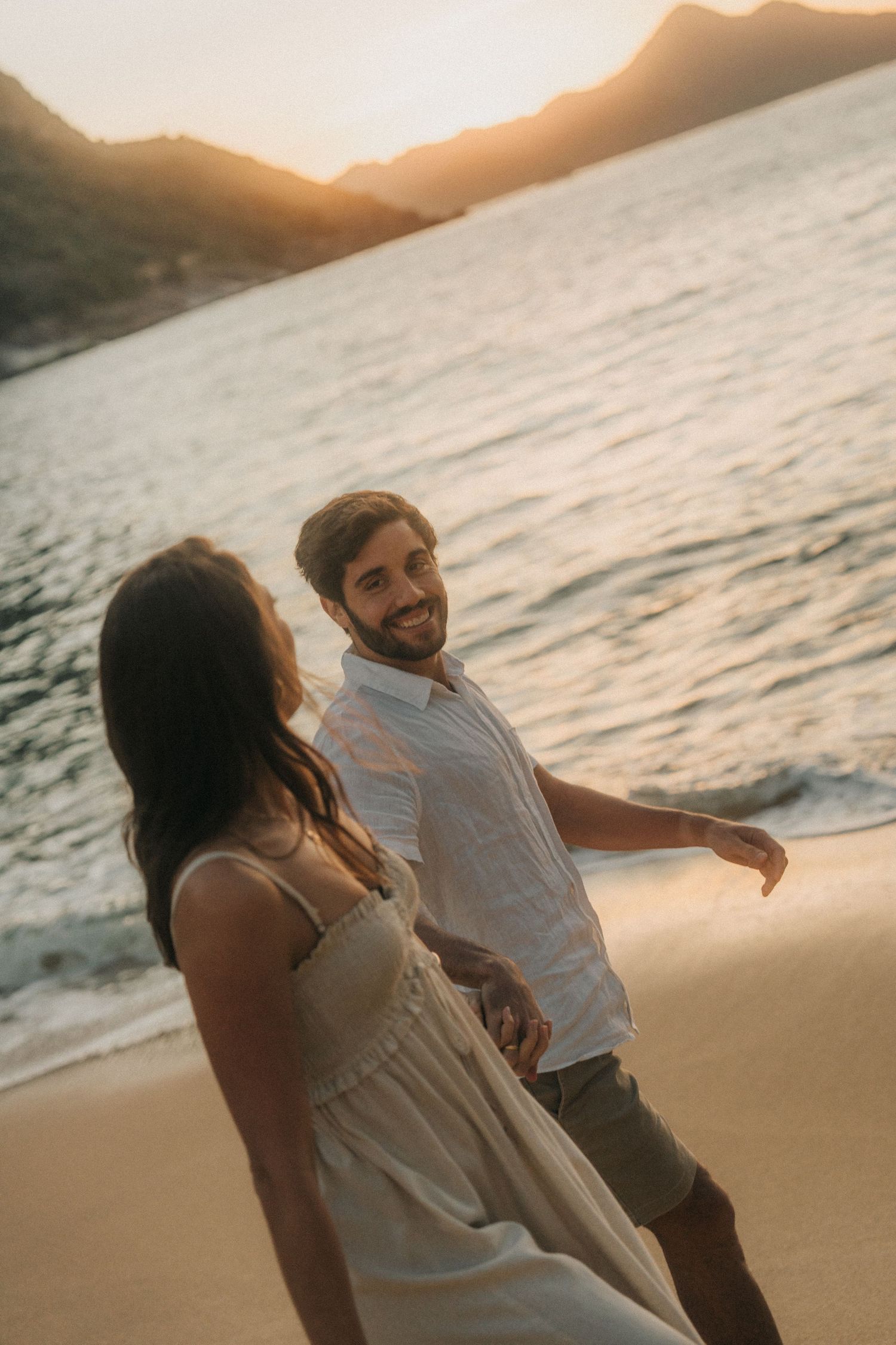 Couple enjoying a romantic moment at sunset on the beach, laughing and playing in golden light on the sand.