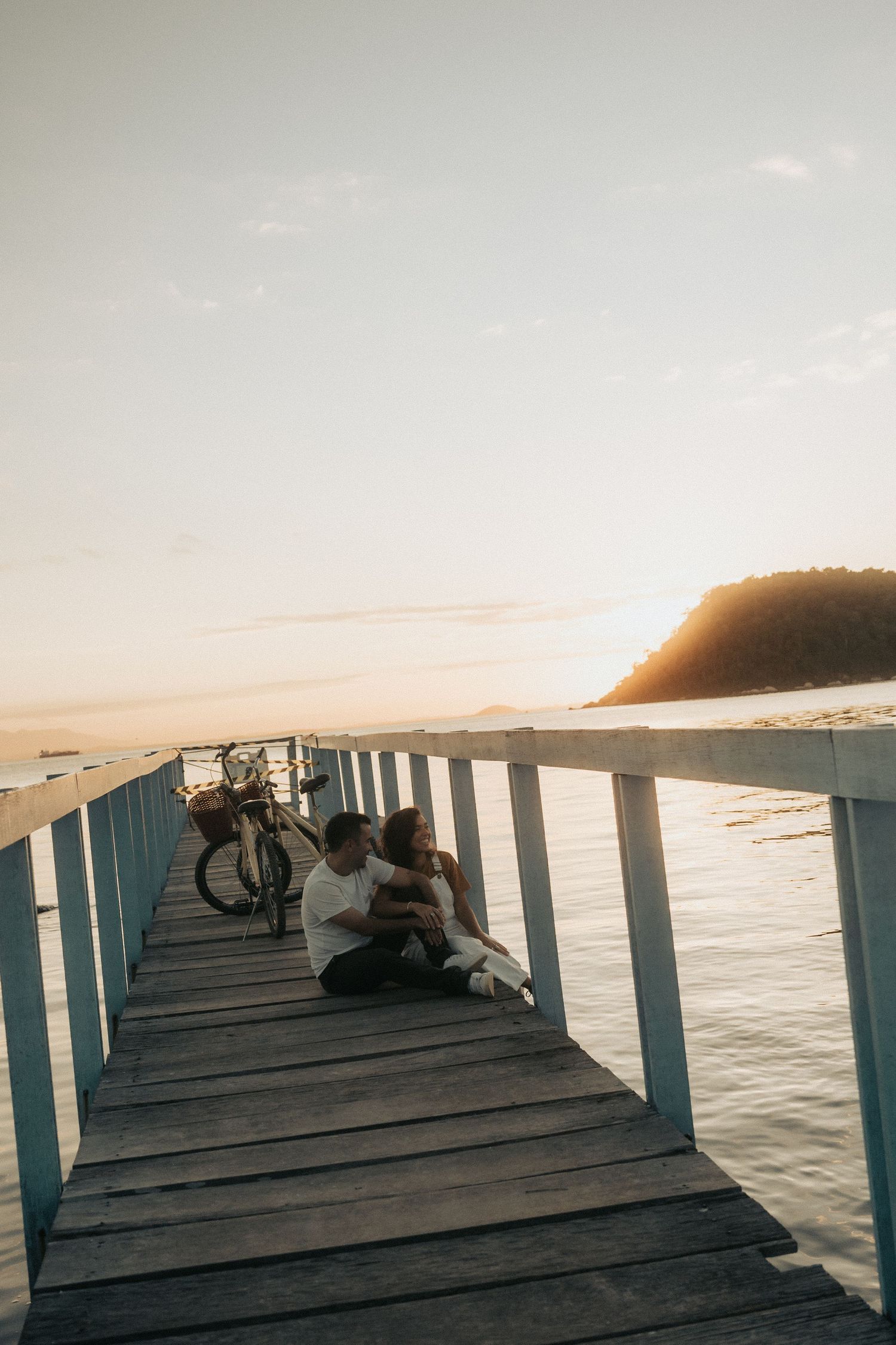 A serene sunset view through a repeating jetty structure stretching across calm waters with people sitting at the edge.