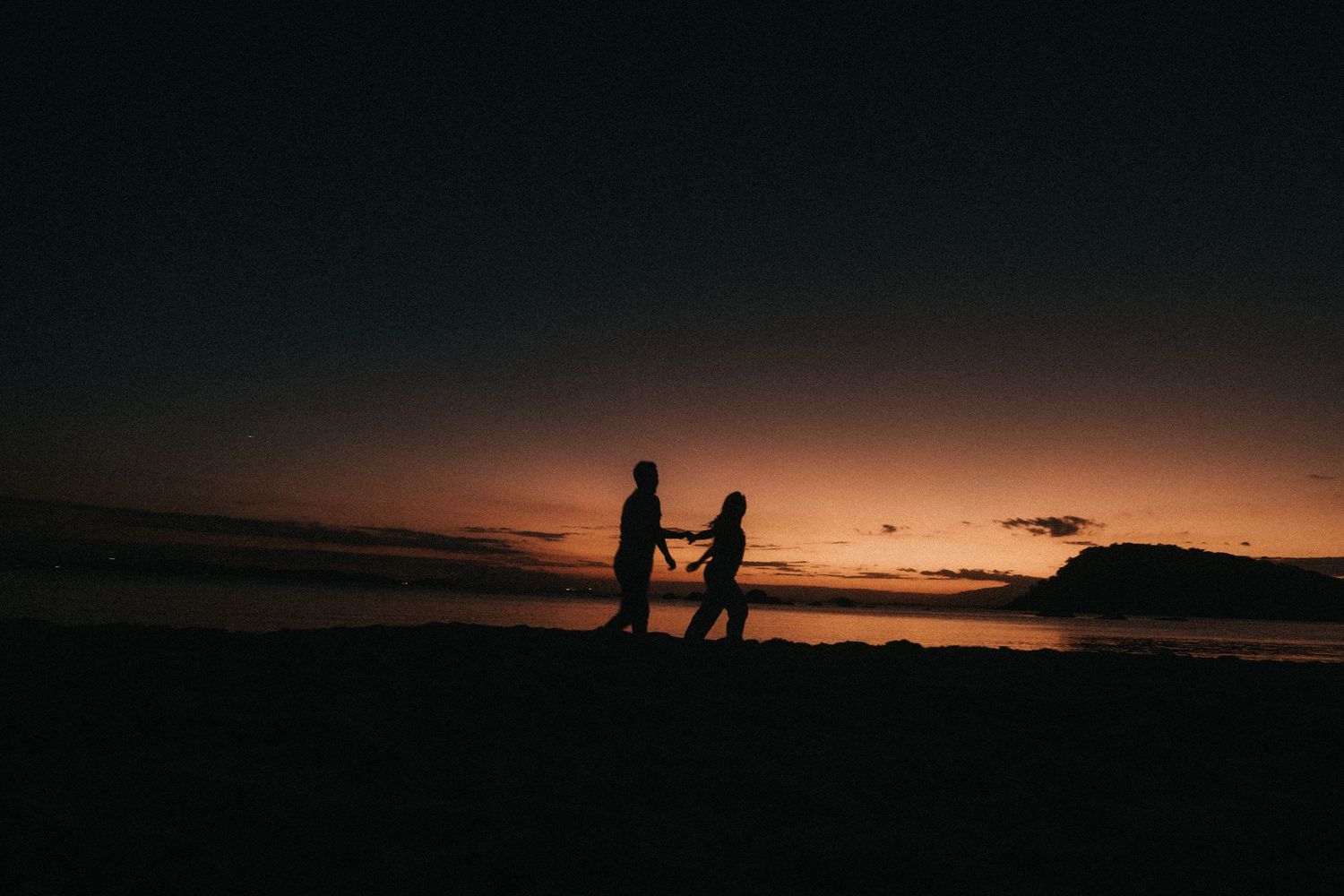 Silhouetted figures stand on a hill against a dramatic orange and purple sunset sky.