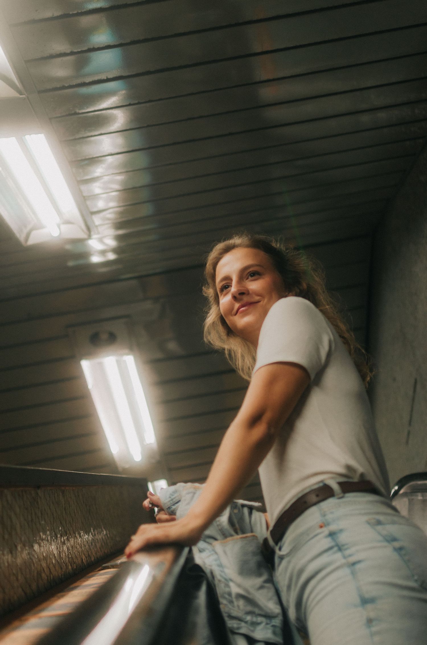 A person in light jeans and a white t-shirt smiles and leans against wooden paneled walls in a series of candid photos.