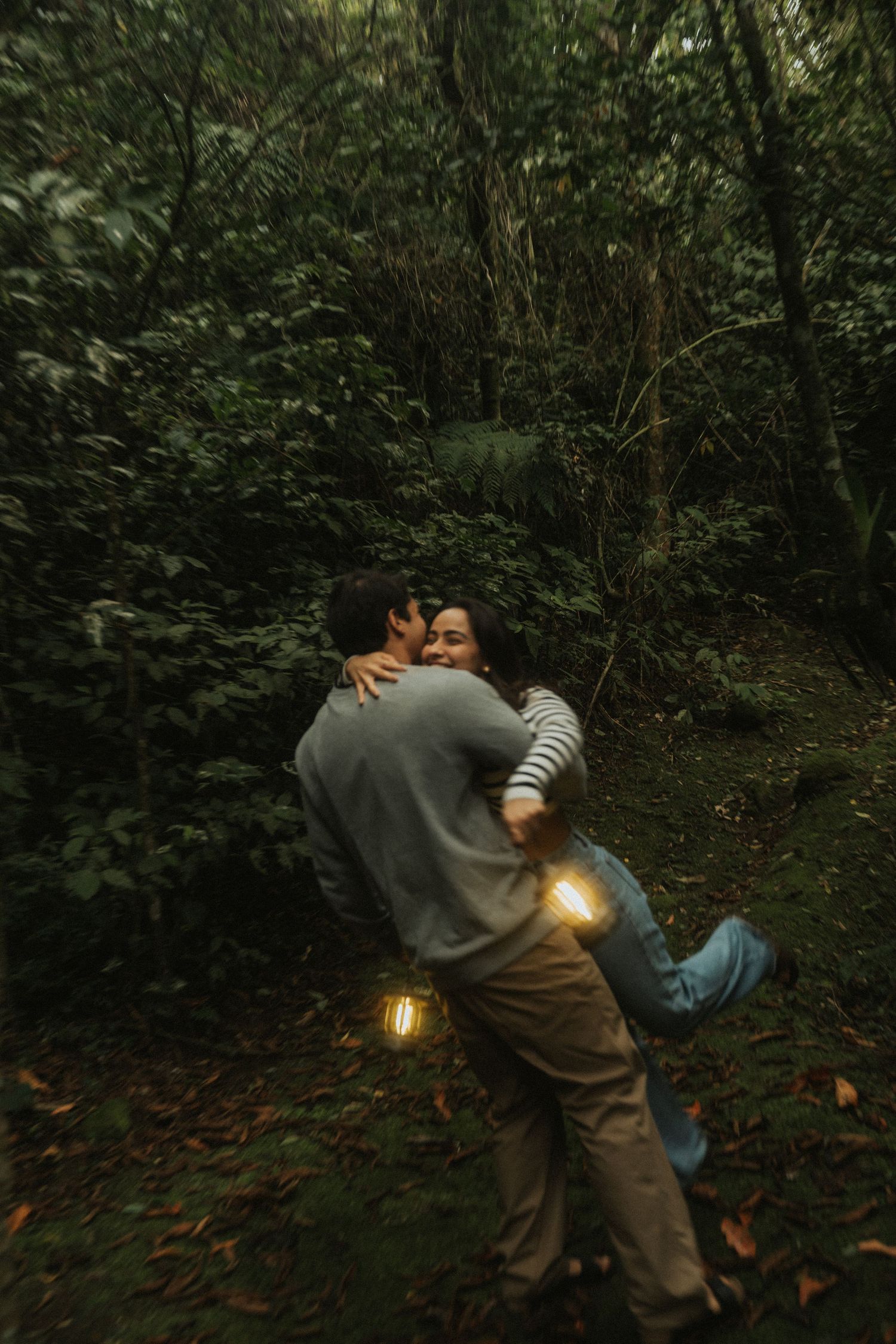Two people explore a dark forest path at night while holding a glowing lantern through a series of progressive shots.