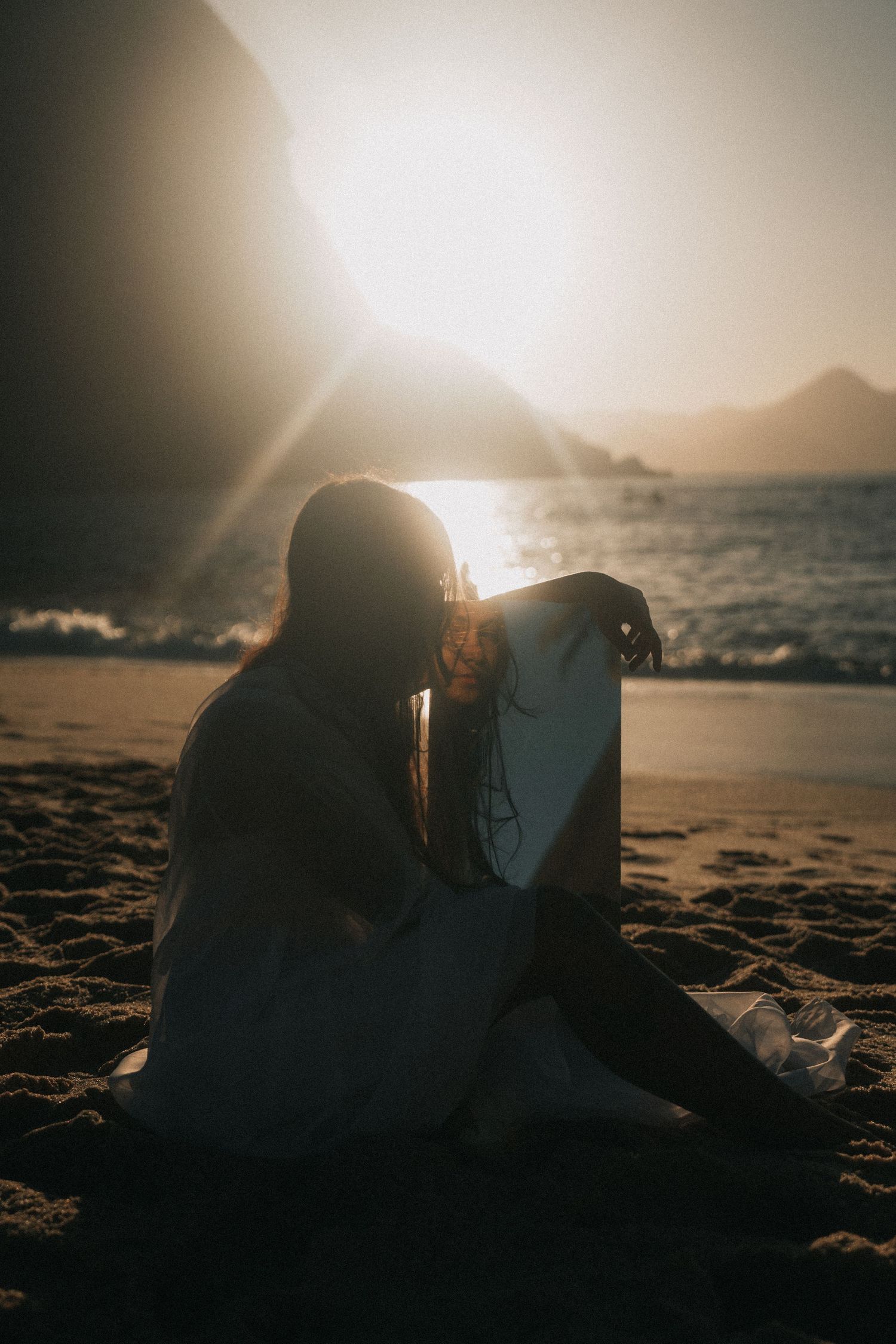 A series of silhouettes sit on the beach during golden sunset, creating a romantic atmospheric scene by the ocean.