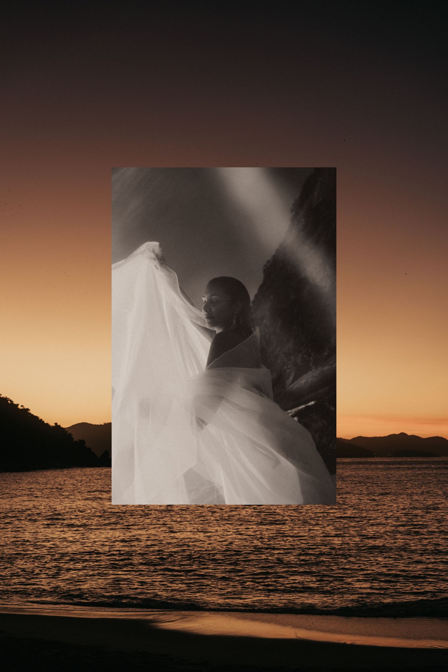 A silhouetted couple embraces by the beach at sunset with a cascading white veil flowing in the breeze.