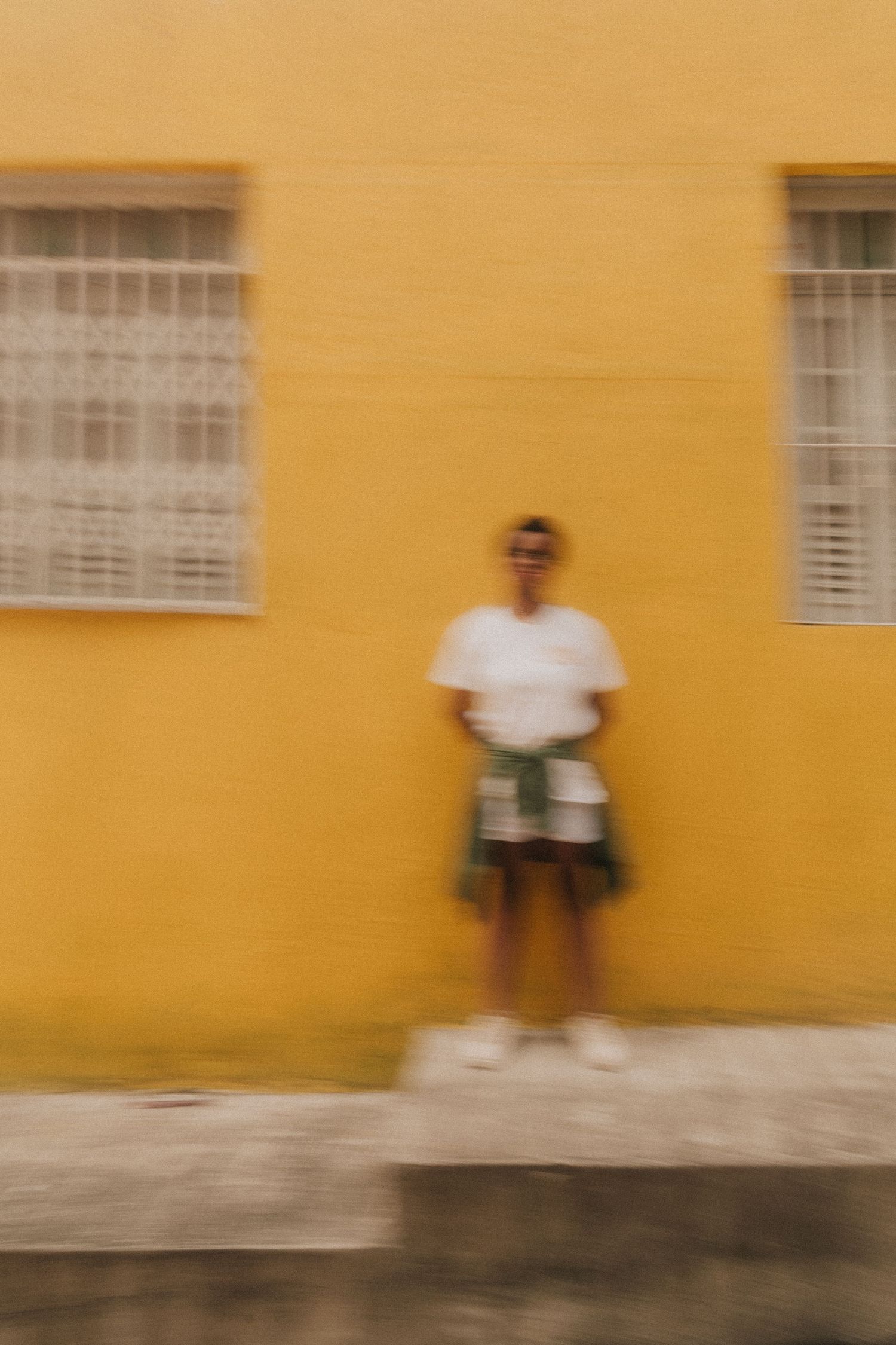 Sequence of motion blur images showing a figure in white against a yellow wall creating an artistic movement effect.