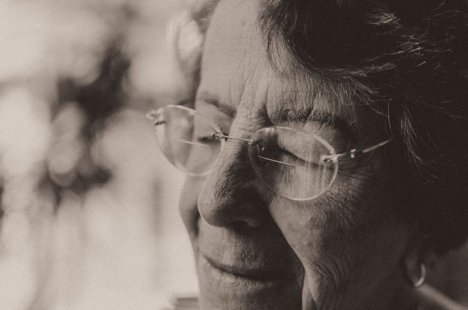A close-up monochrome portrait showing someone wearing glasses in soft lighting with a gentle smile.